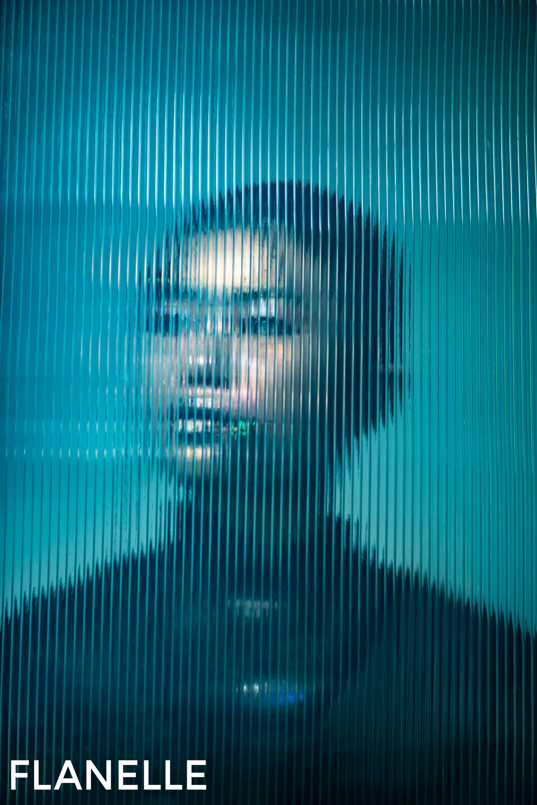 Person blurred behind textured glass, creating a mysterious blue-toned portrait.