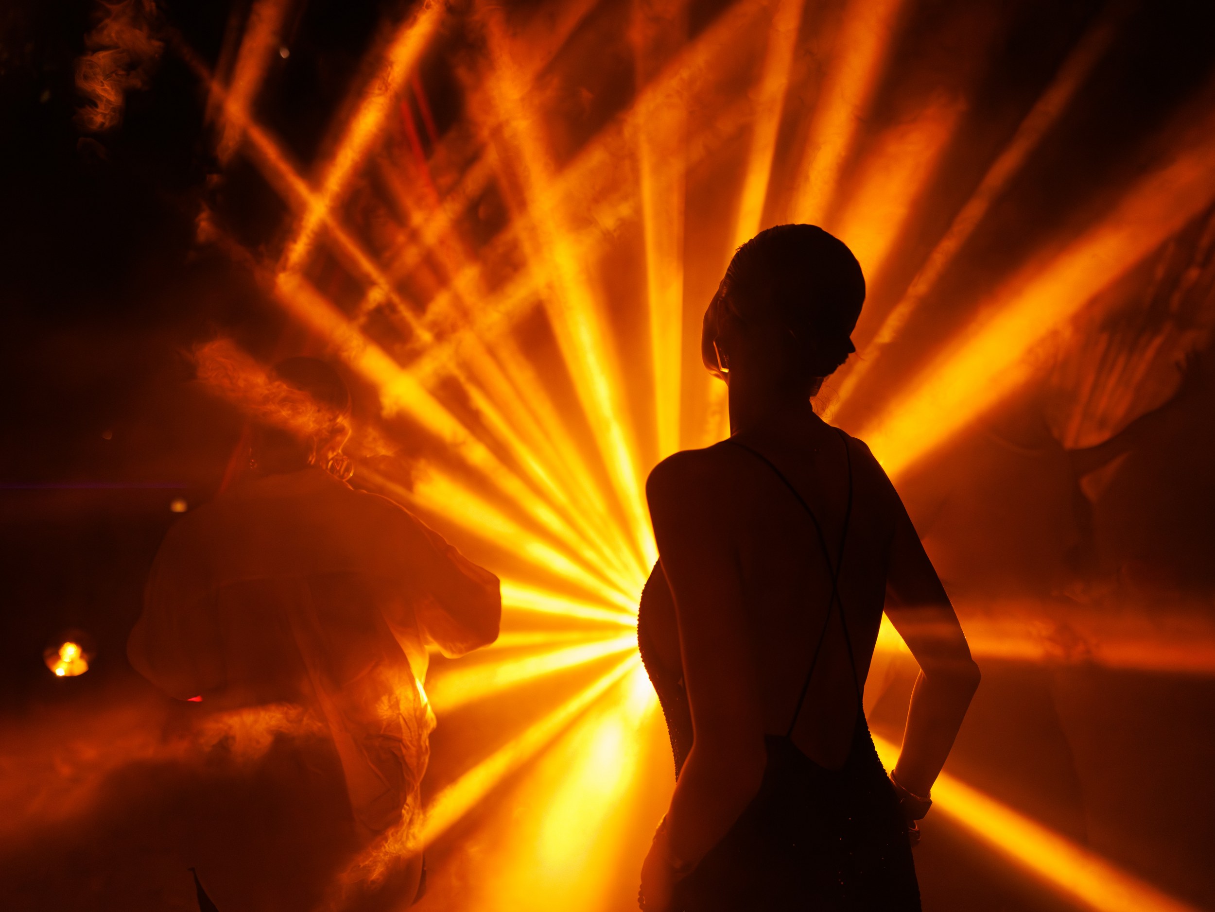 Silhouette dancing in vibrant orange lights at a dynamic party scene.