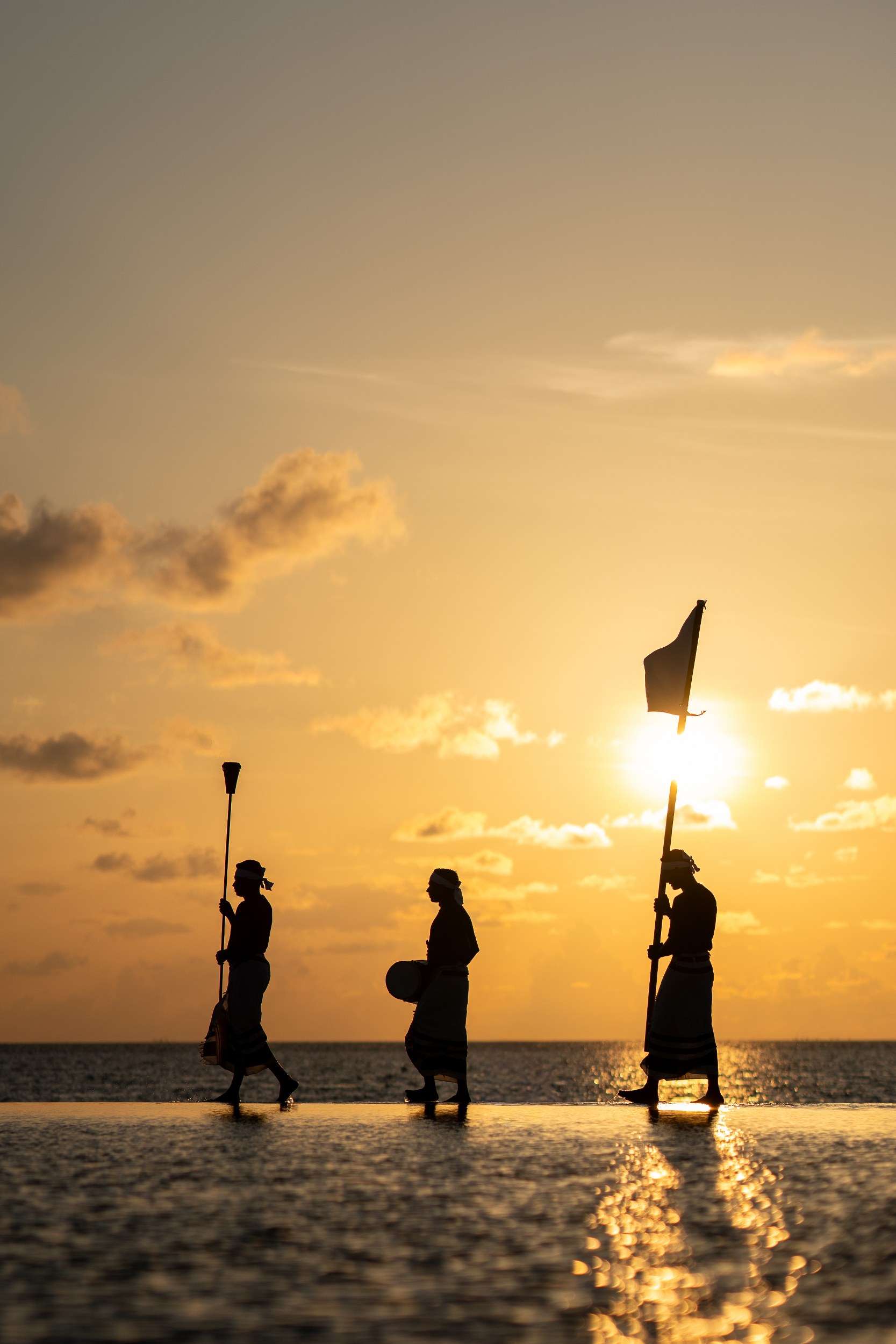 Silhouettes of three people marching at sunset by the water.