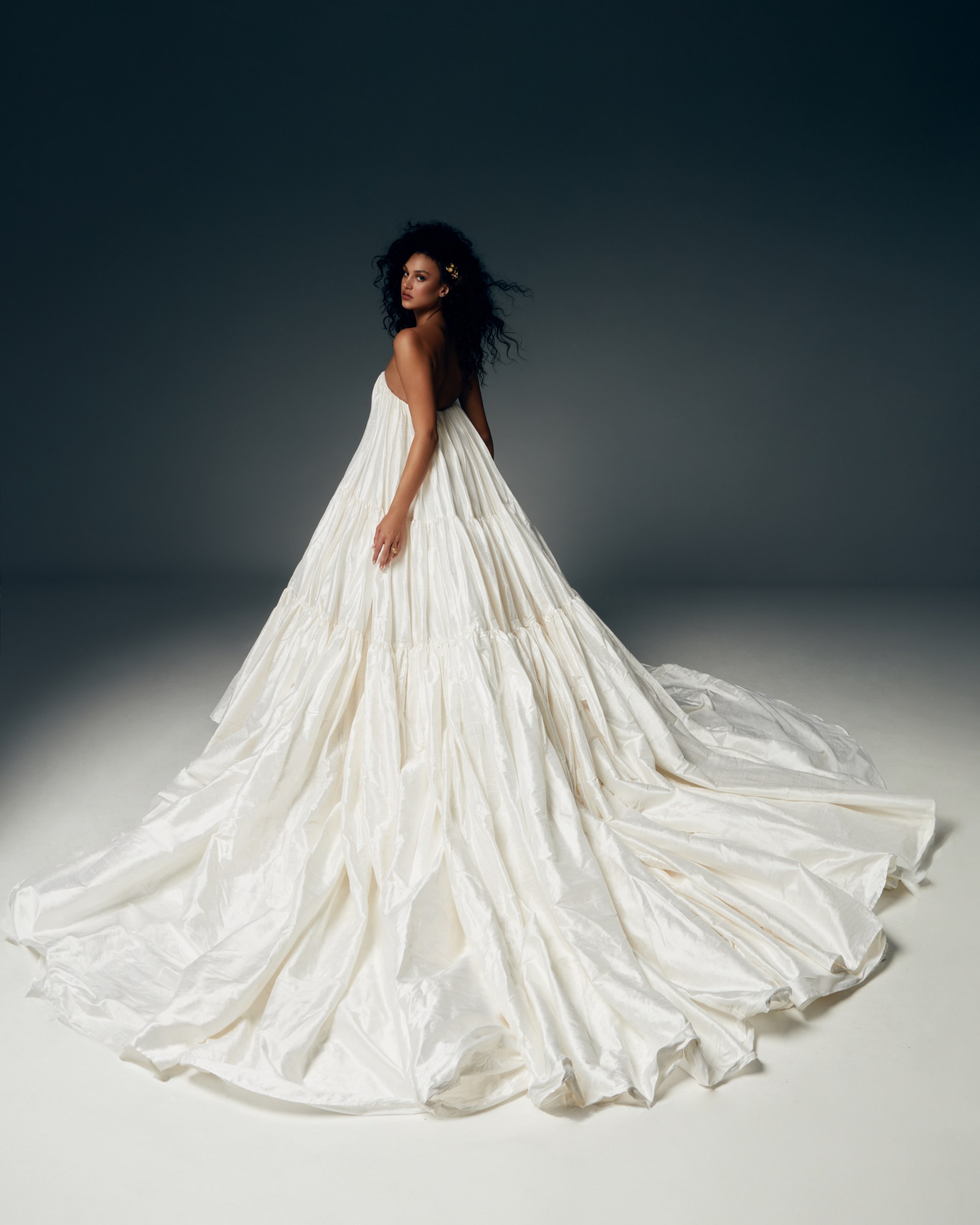 Elegant woman in flowing white gown with dark backdrop, showcasing grand elegance.