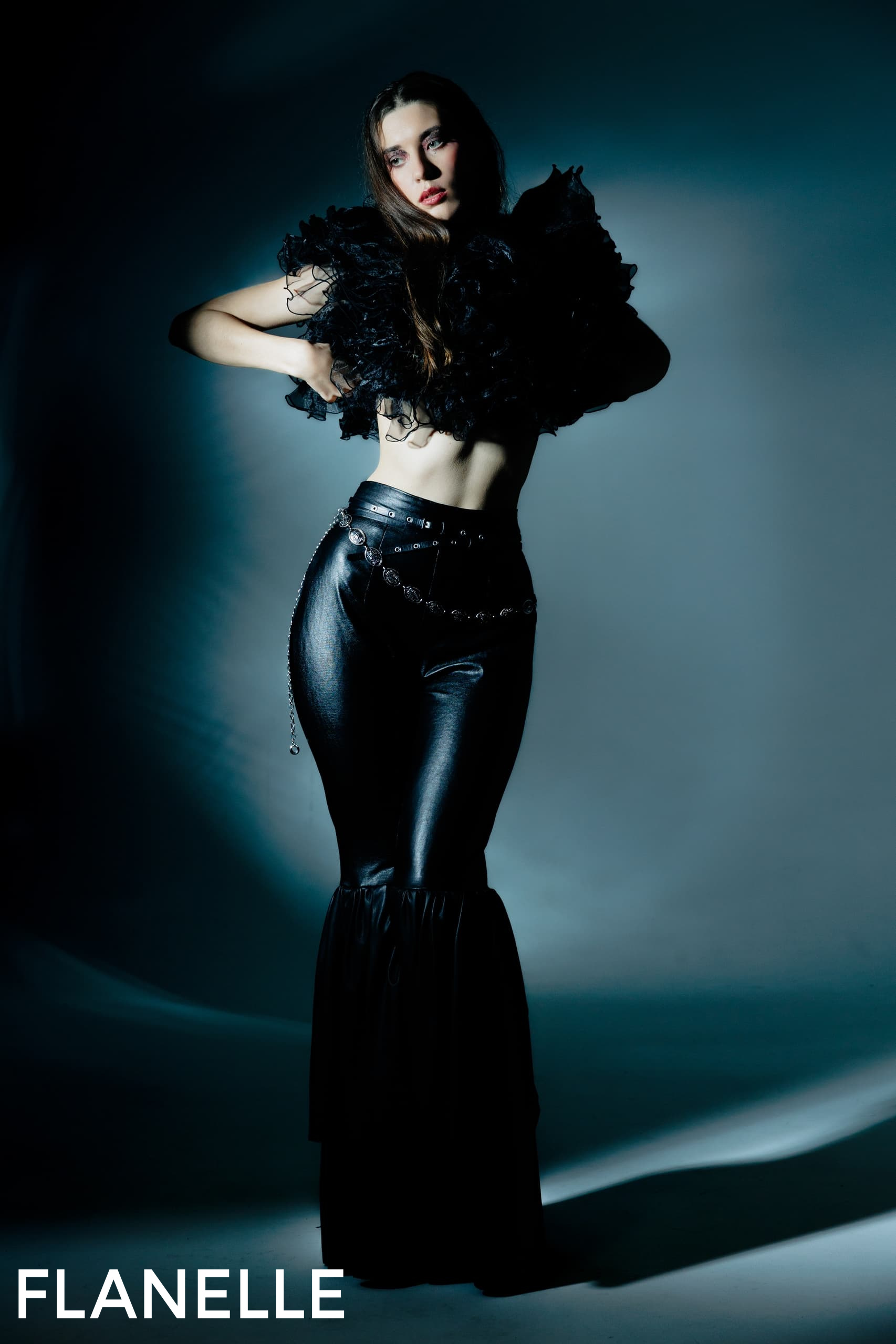 Model wearing black high-fashion outfit with dramatic lighting.
