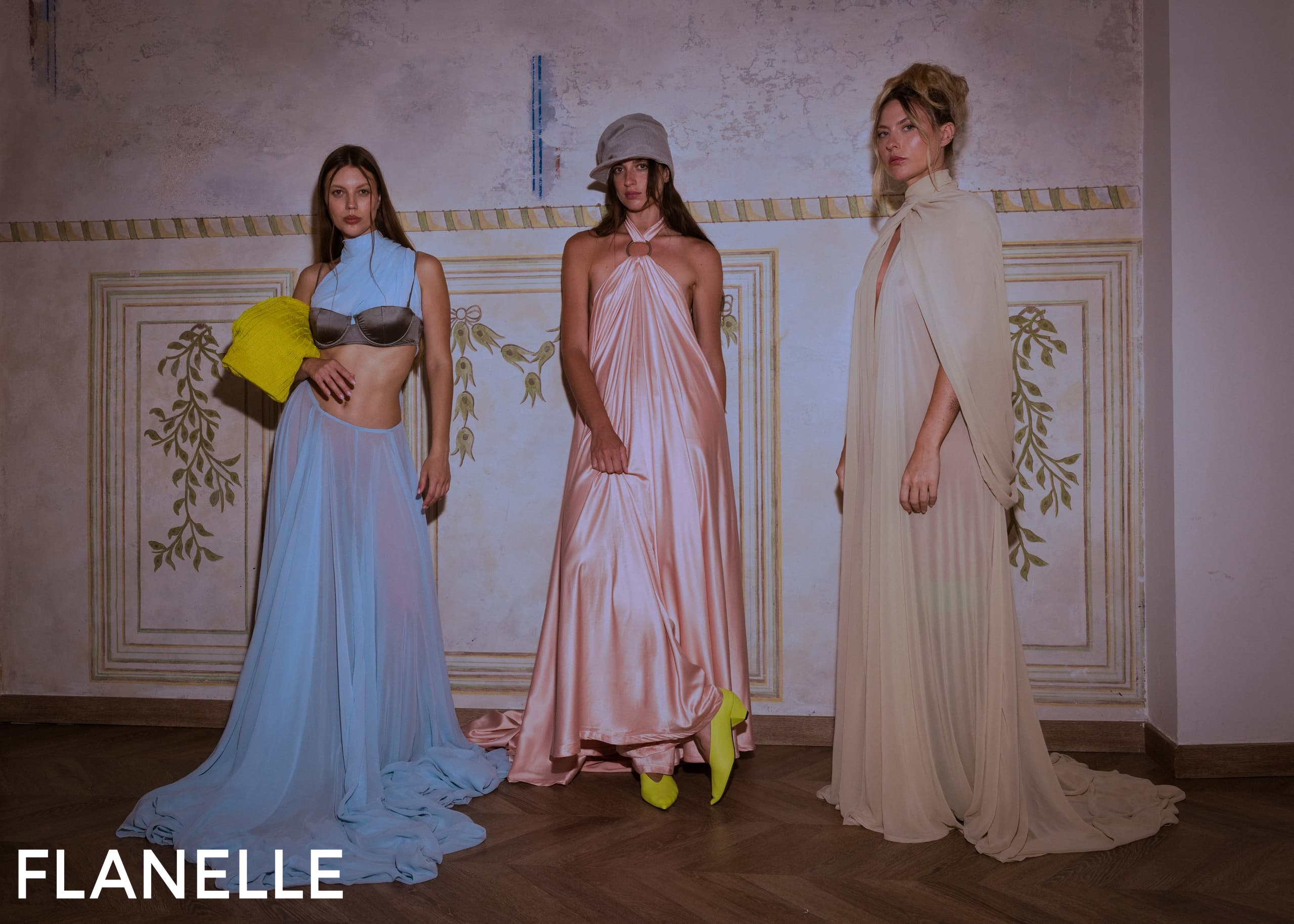 Three models showcase elegant flowing dresses in soft pastel hues.
