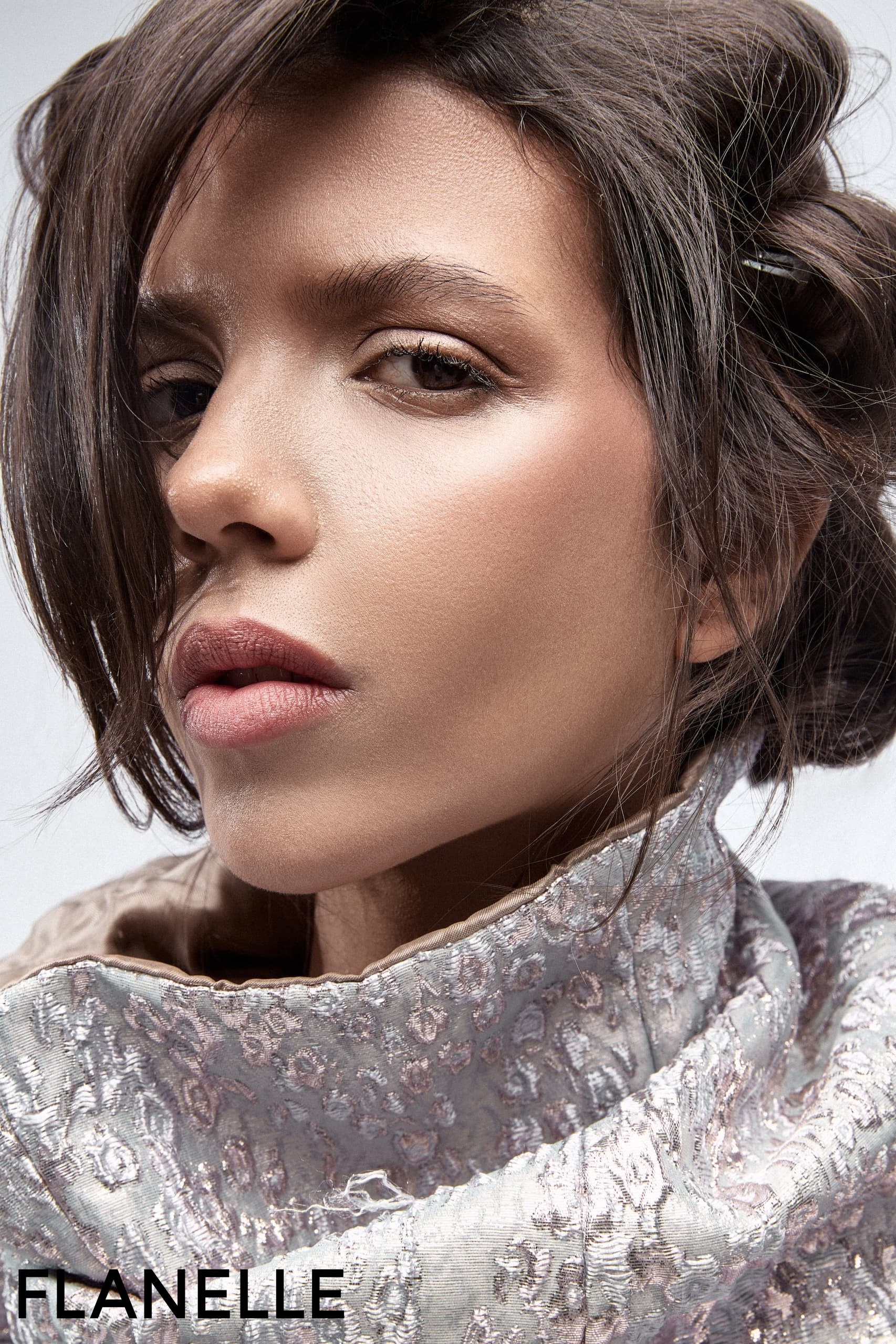 Close-up of a woman with elegant makeup and hairstyle, wearing a textured scarf.