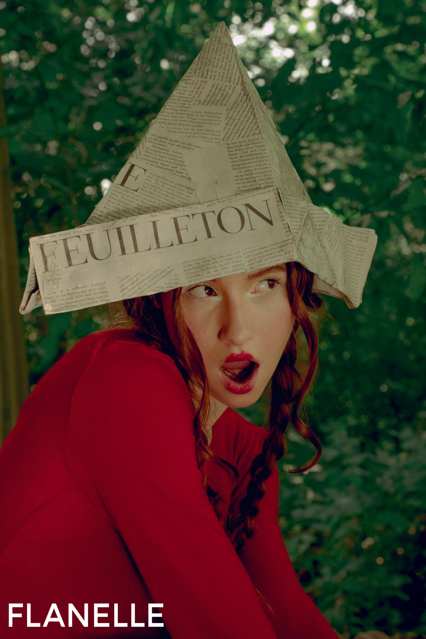 Woman in red dress wearing newspaper hat, forest background. Fashion editorial shot.