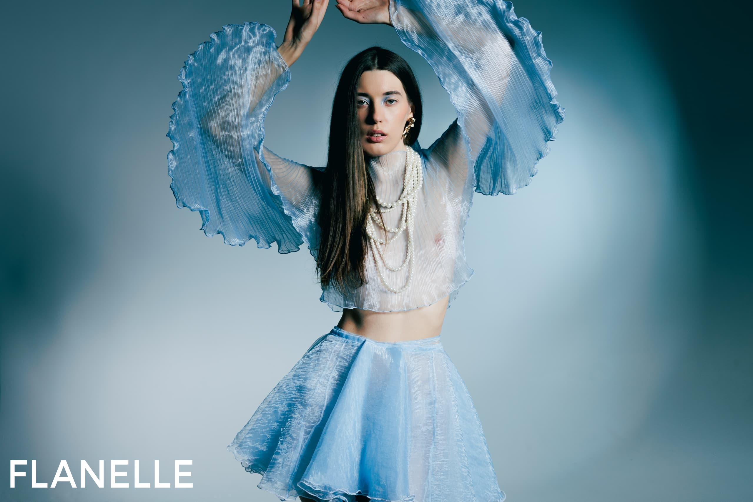 Fashion model in blue sheer outfit with ruffled sleeves, elegant and stylish.