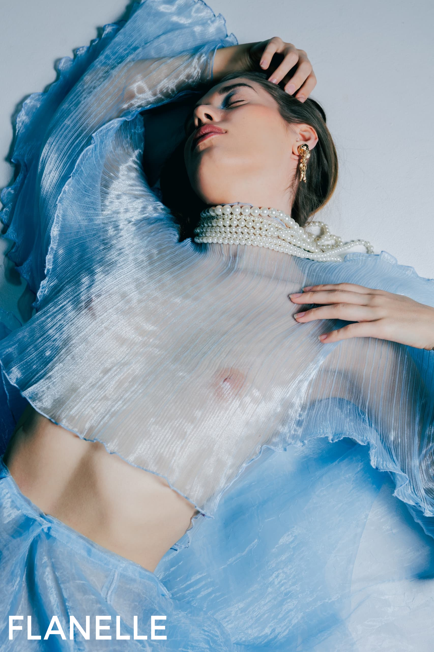 Person in sheer blue dress and pearl necklace, artistic fashion photography.