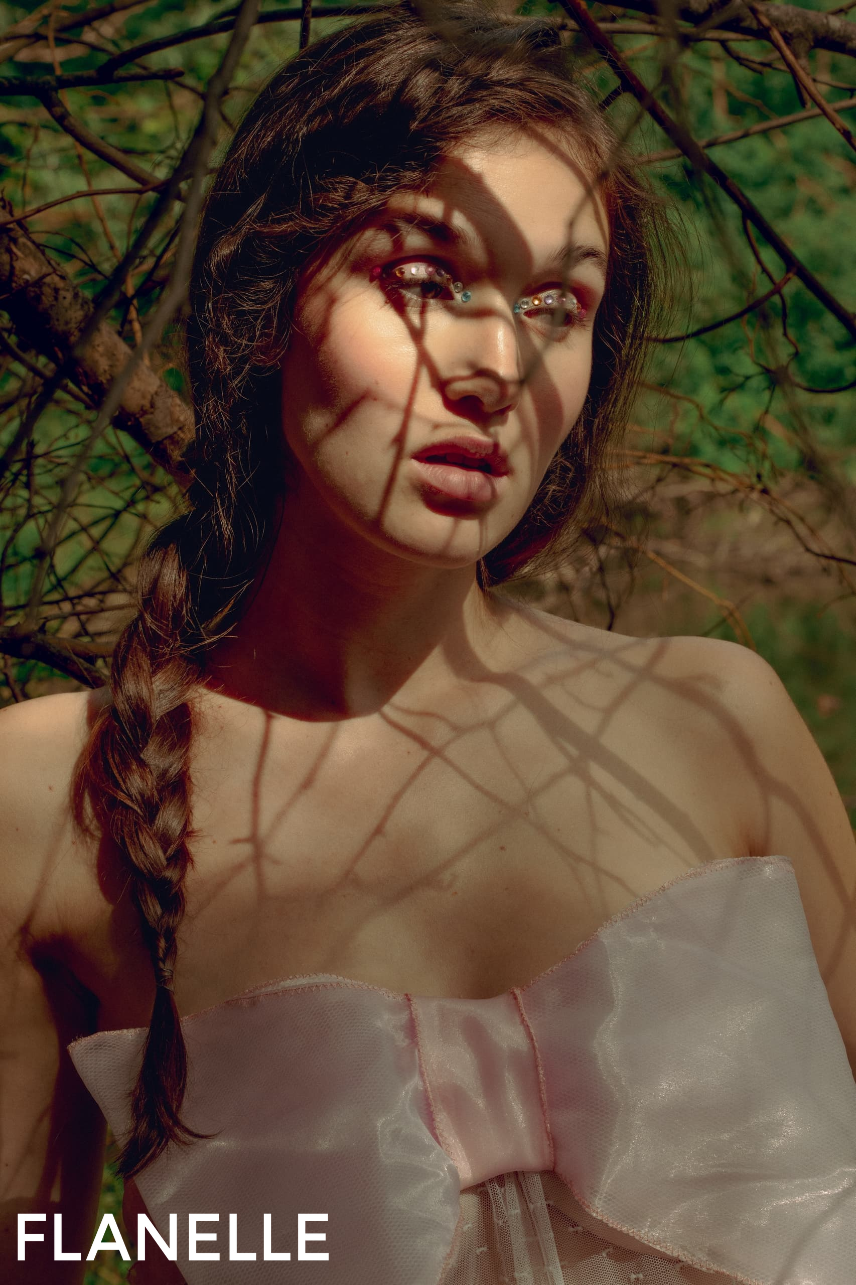 Woman in forest shades with braided hair and pink bow dress, artistic portrait.