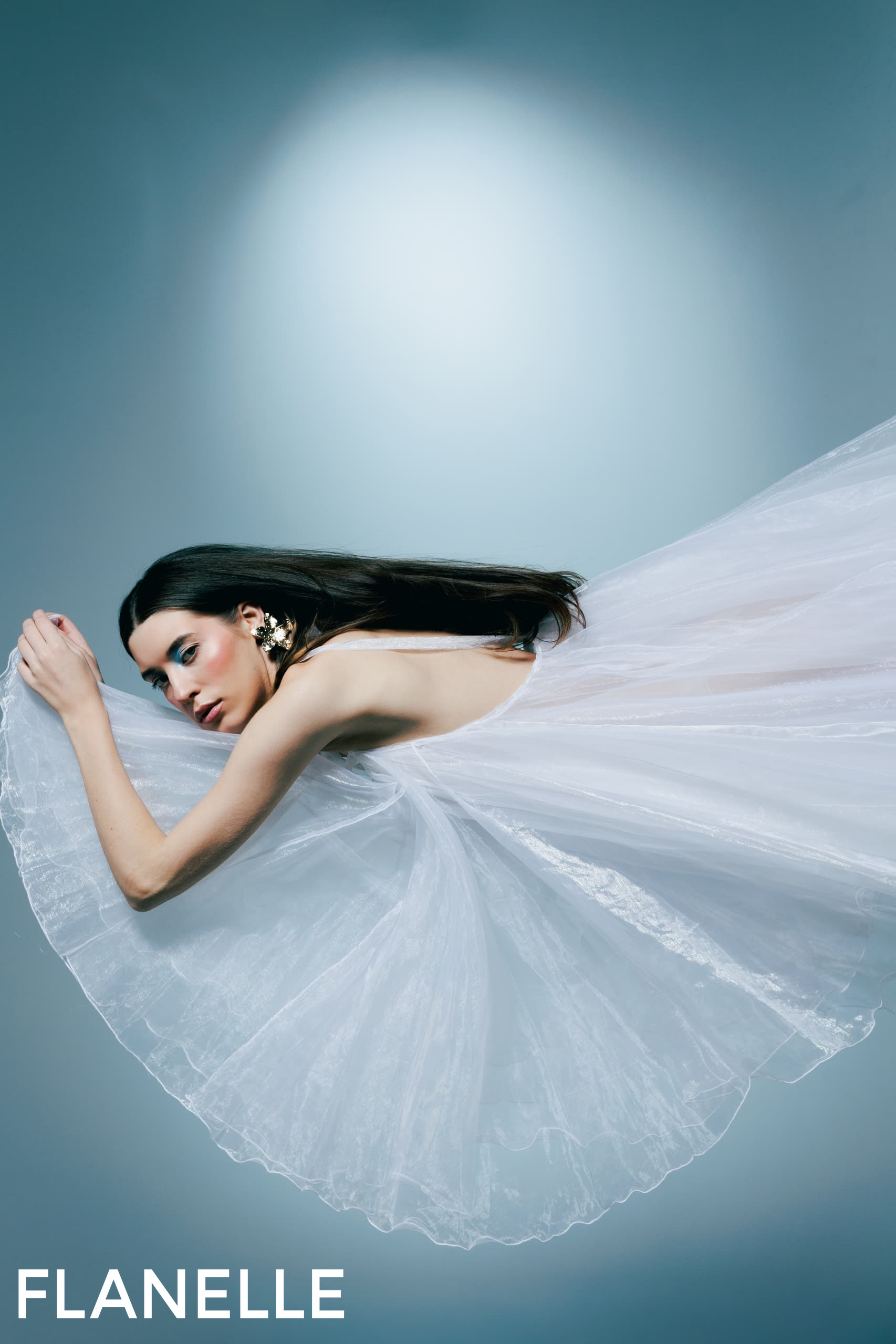 Elegant woman in flowing white dress against blue background.