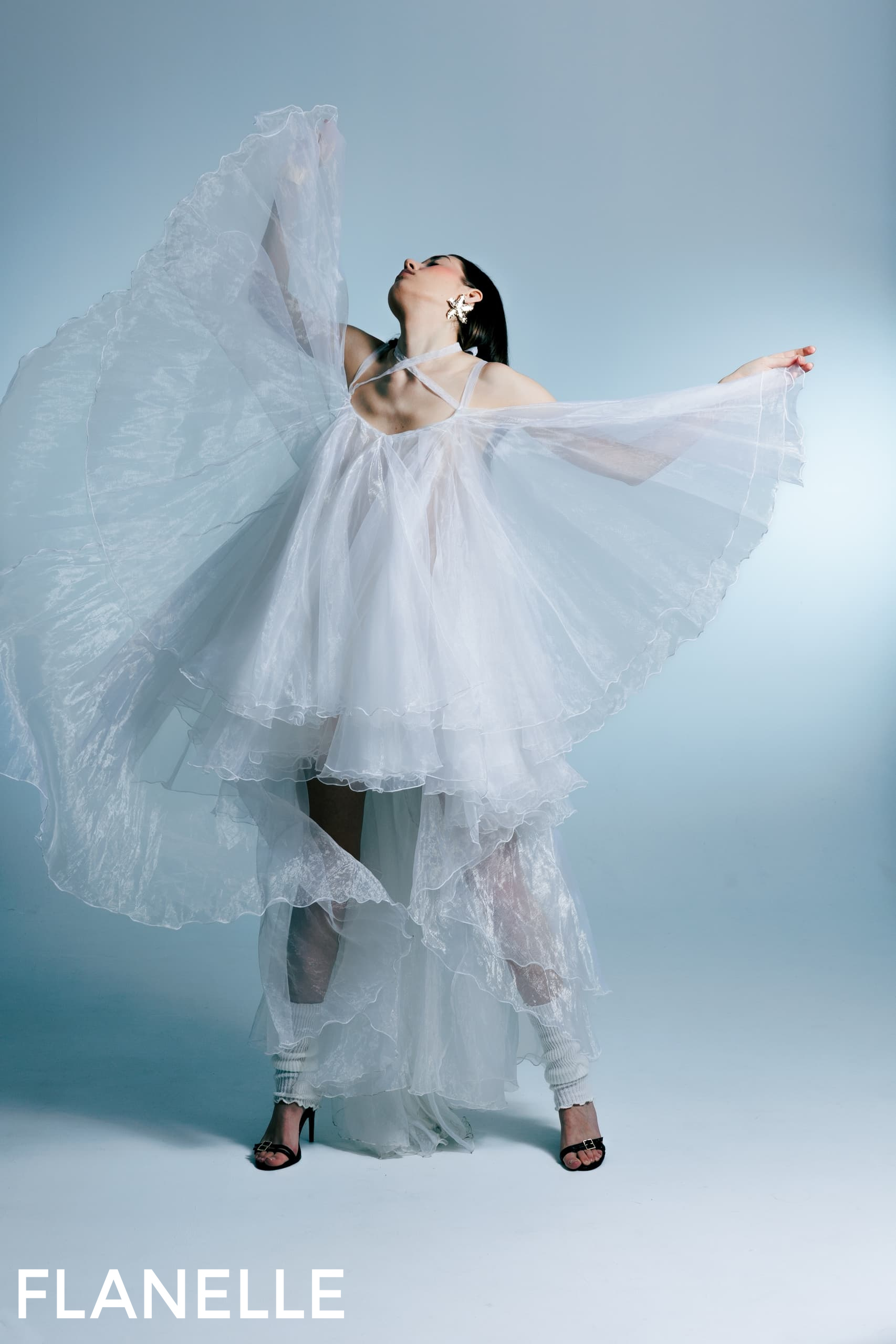 Elegant model in flowing white dress with dramatic pose on blue background.