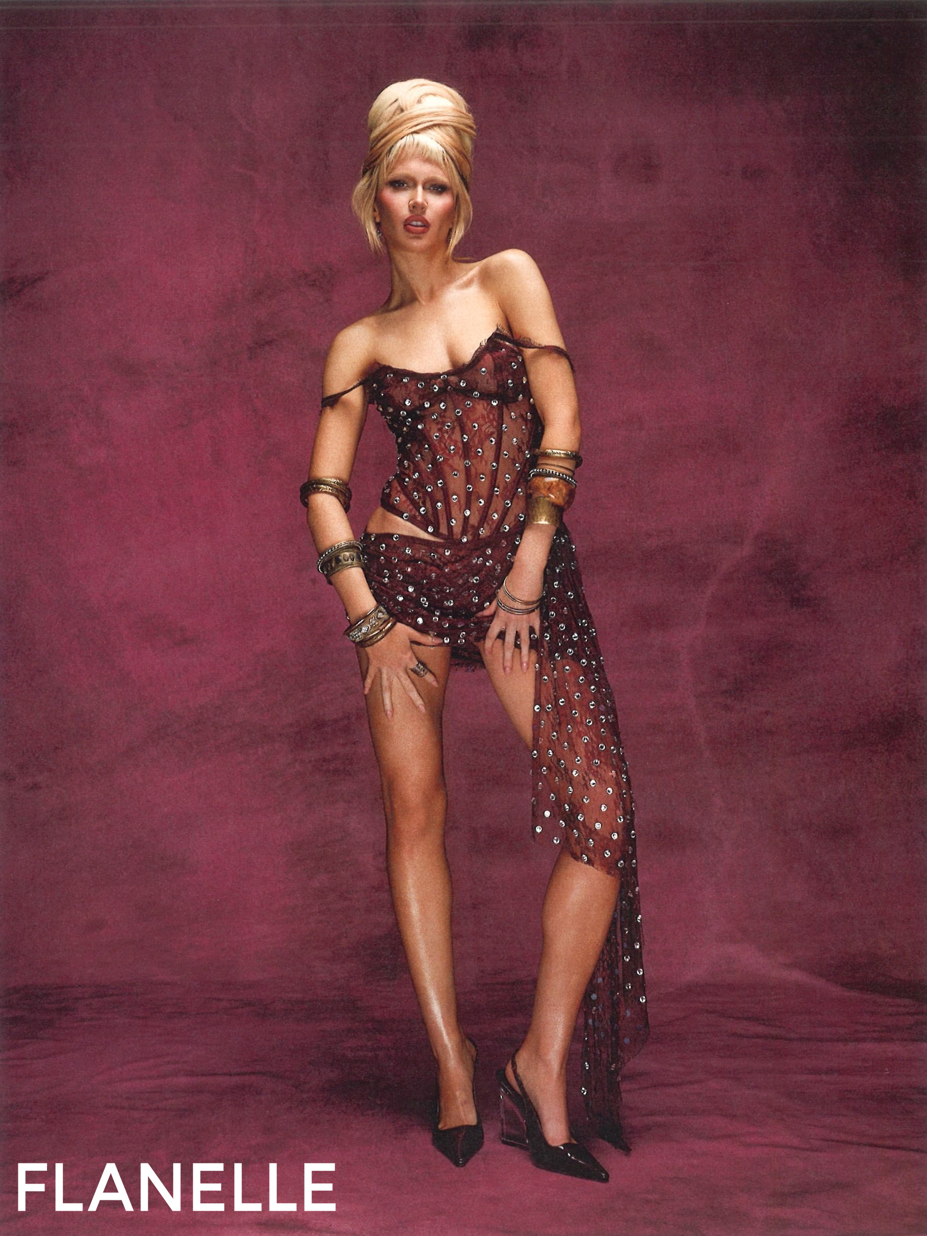Woman in stylish sheer dress poses against a burgundy background.
