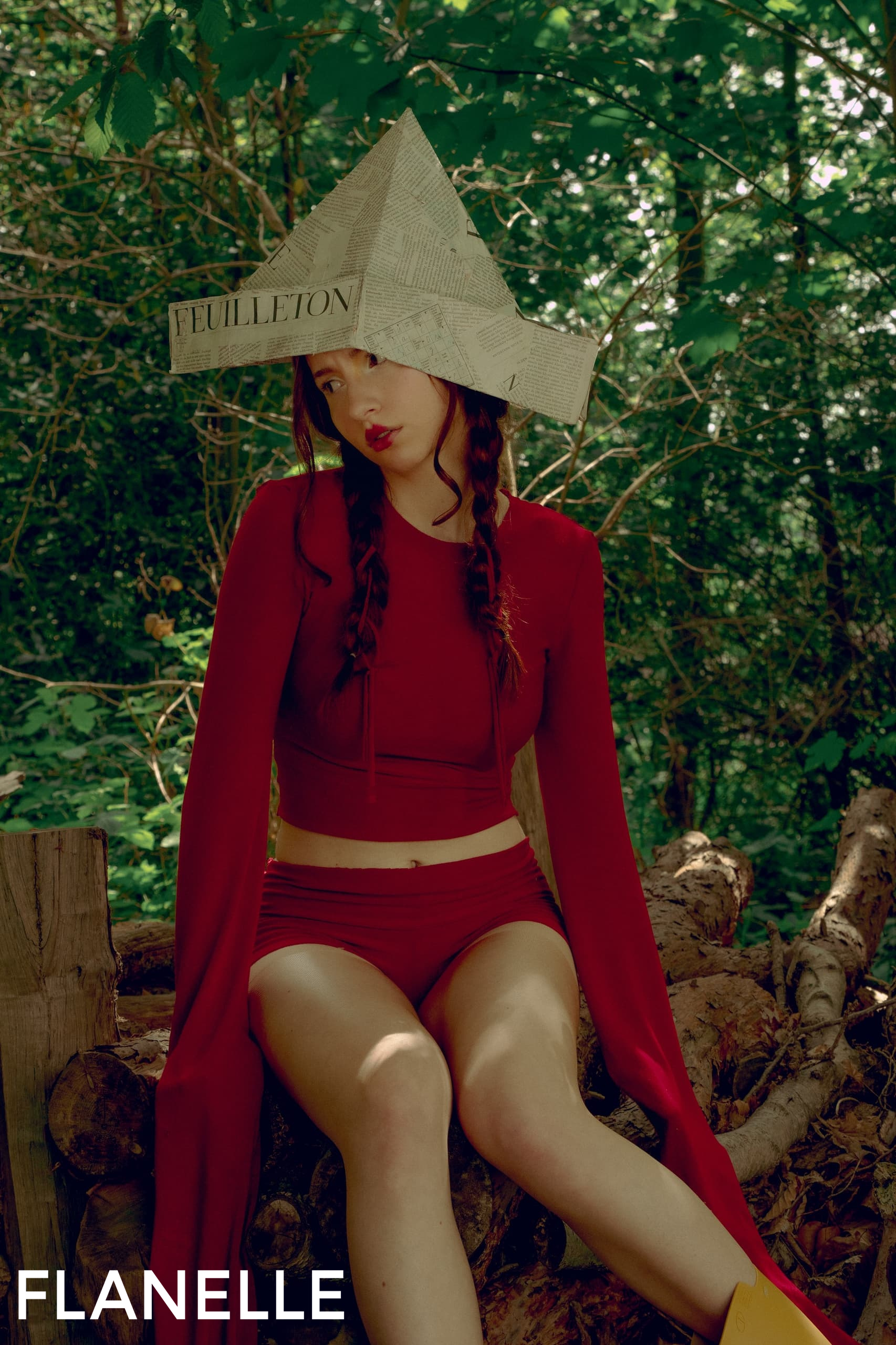 Woman in red with paper hat sitting in a forest setting.