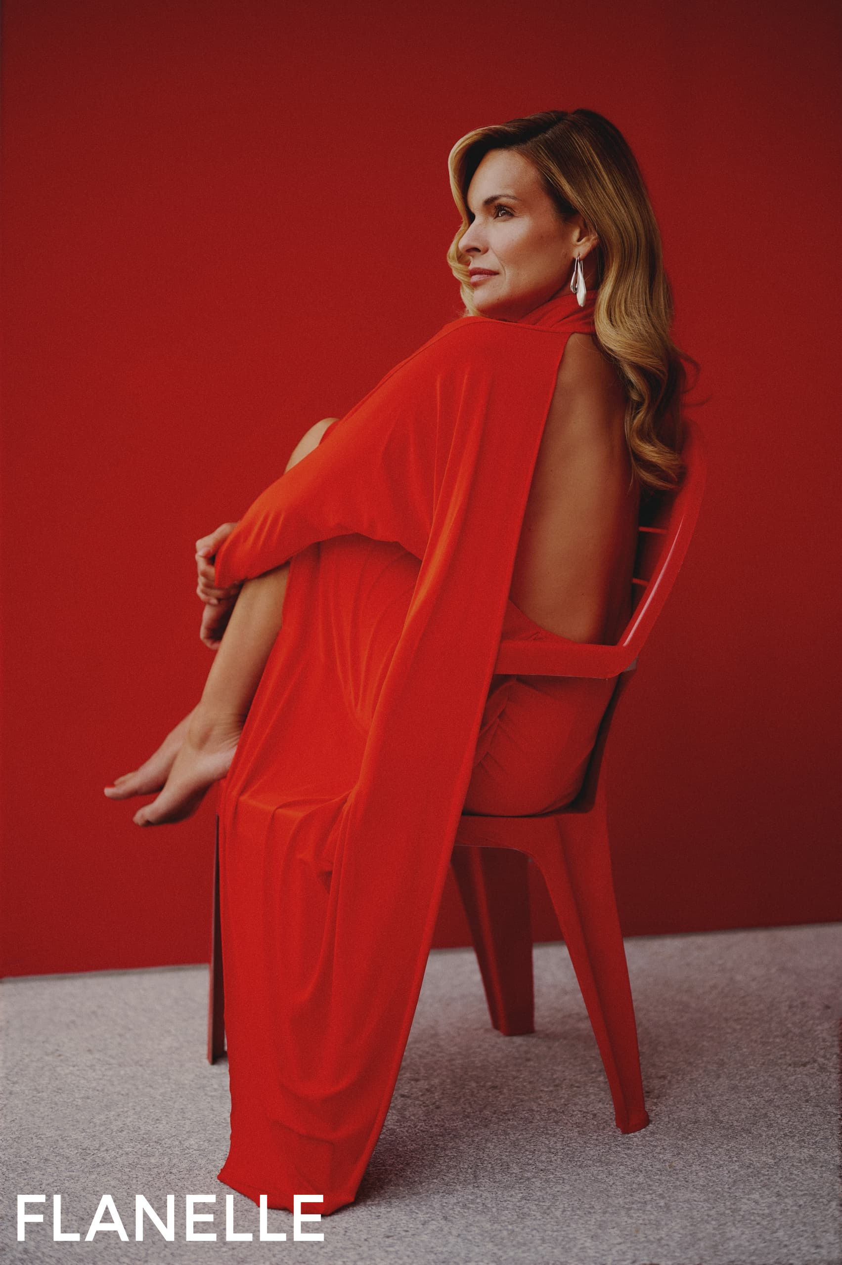 Woman in red dress sitting on chair against red background