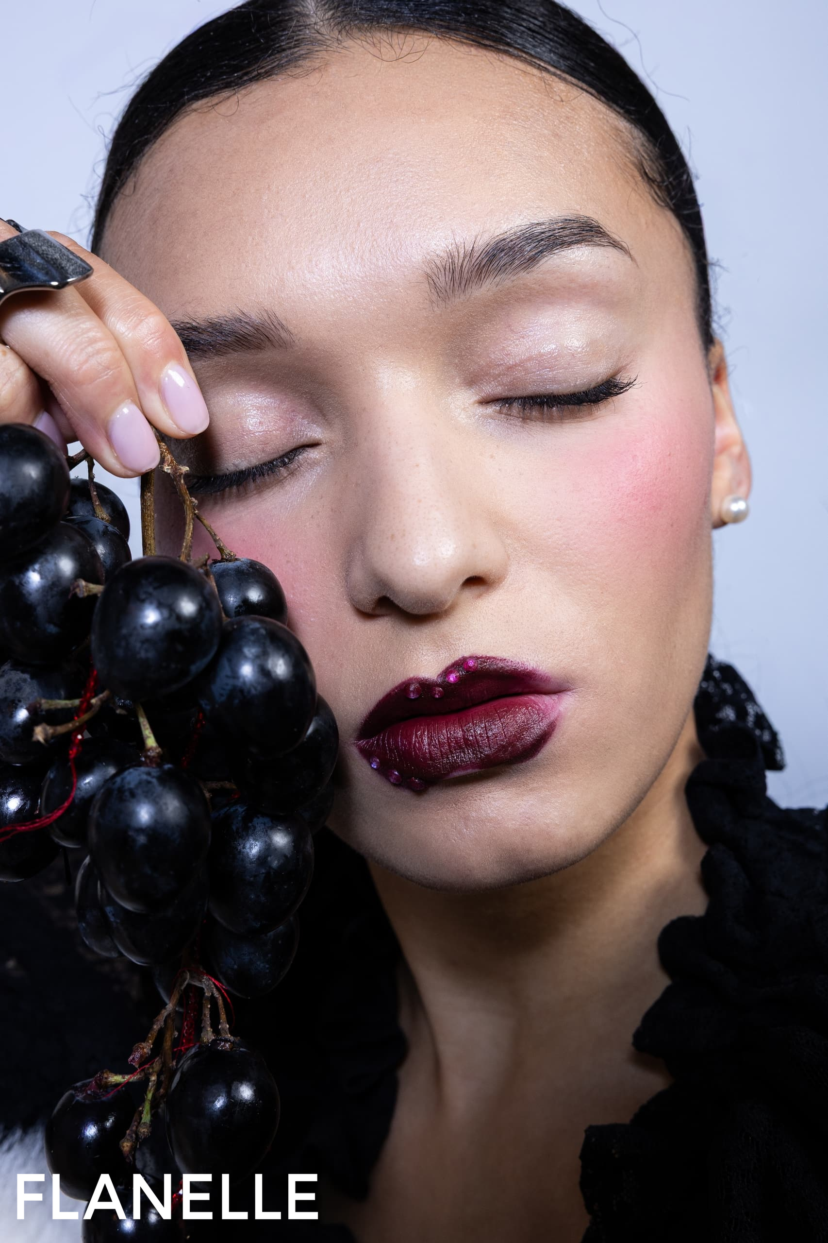 Woman with dark lipstick and grapes, elegant beauty shot.