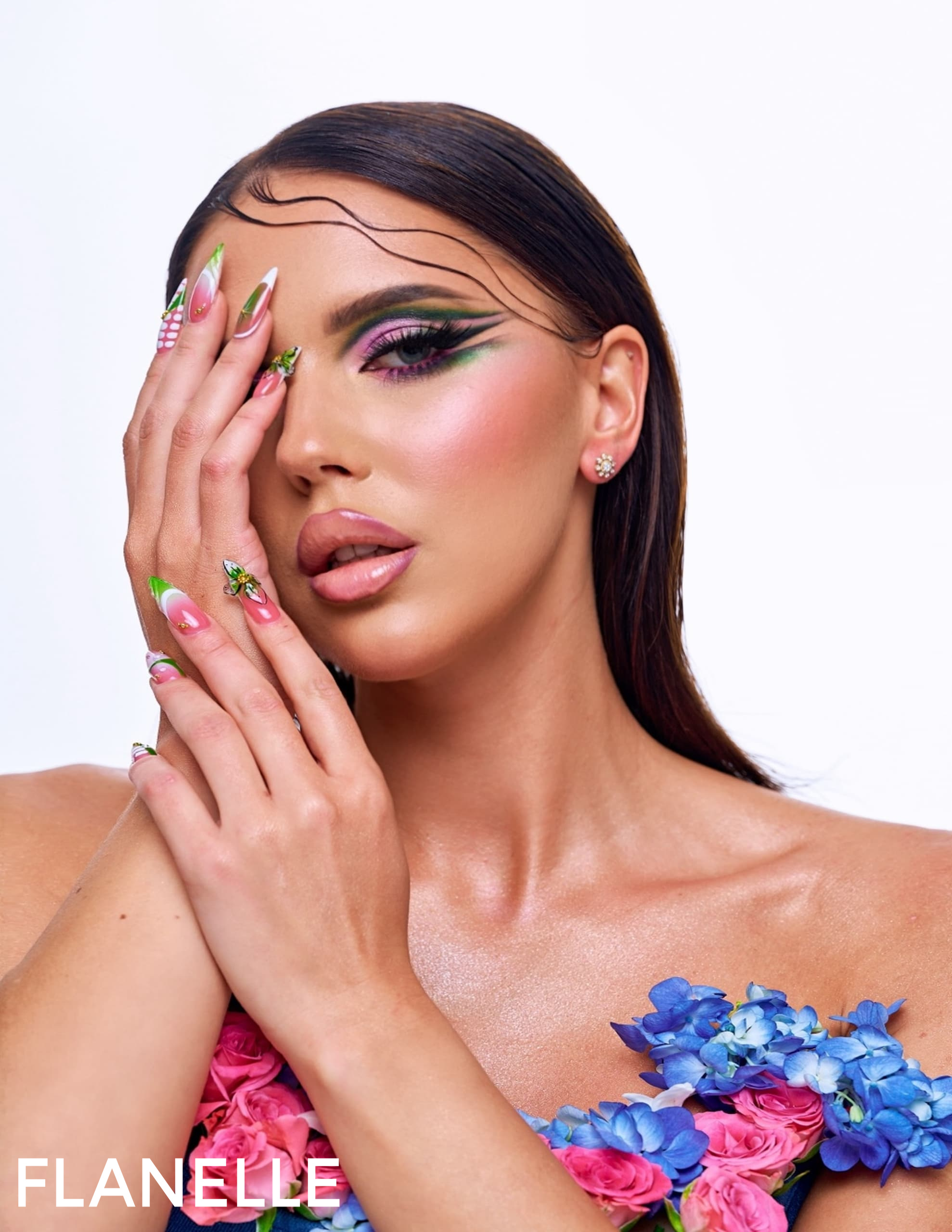 Model with vibrant makeup and floral dress against white background. Bold eye look.