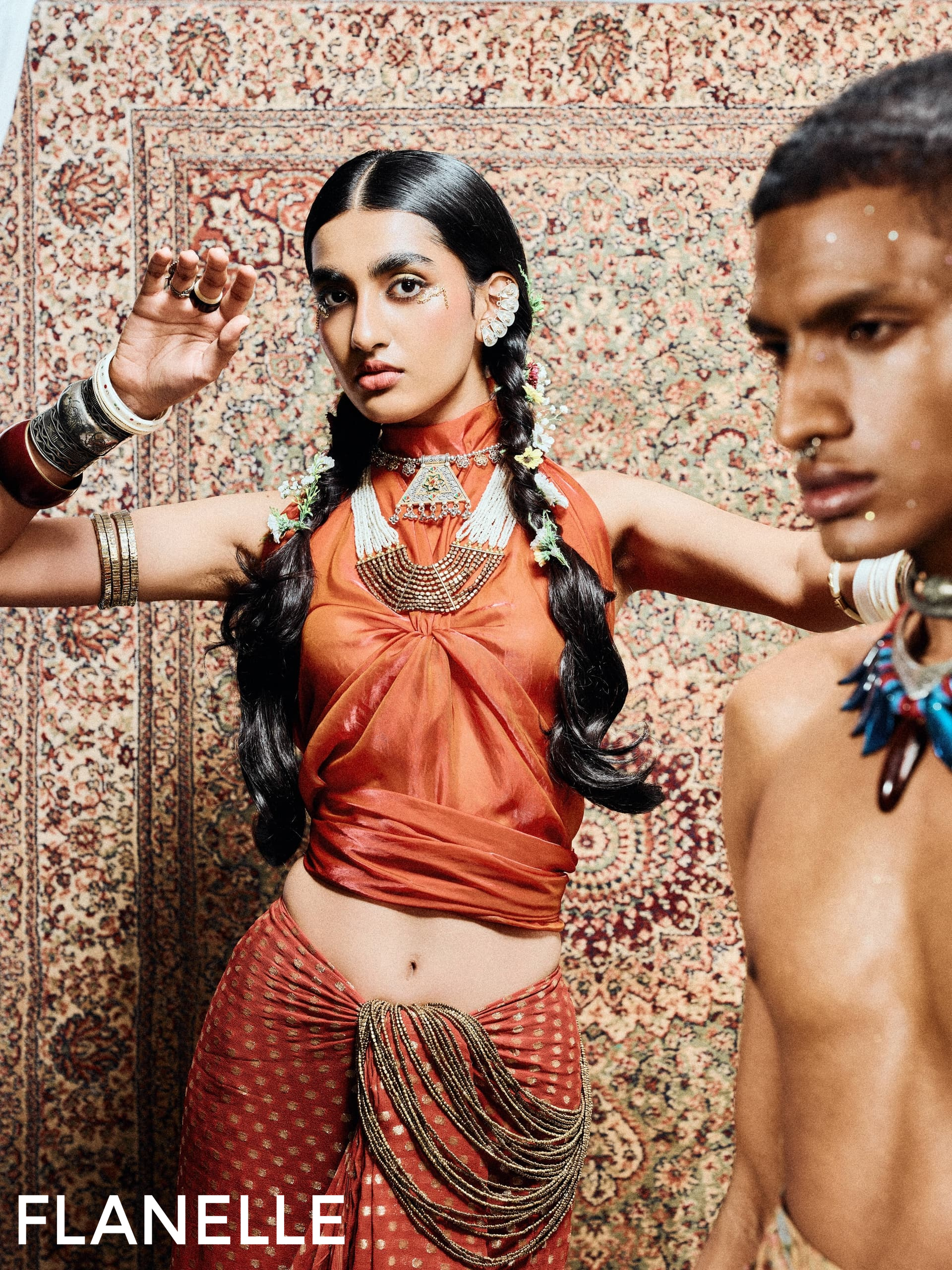 Fashion editorial with ornate jewelry and vibrant attire against patterned backdrop.