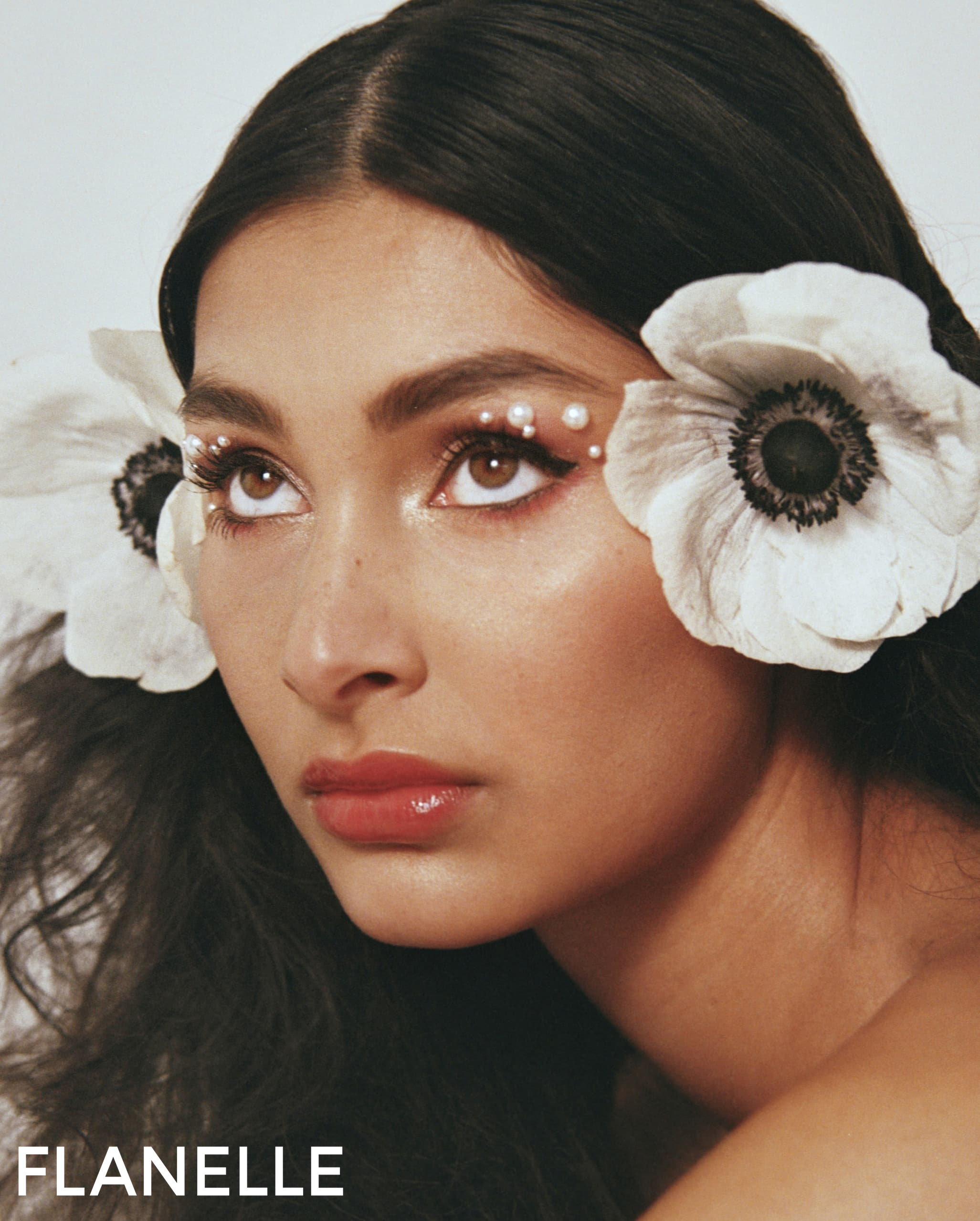 Woman with floral headpiece and creative makeup, featuring white flowers and pearls.