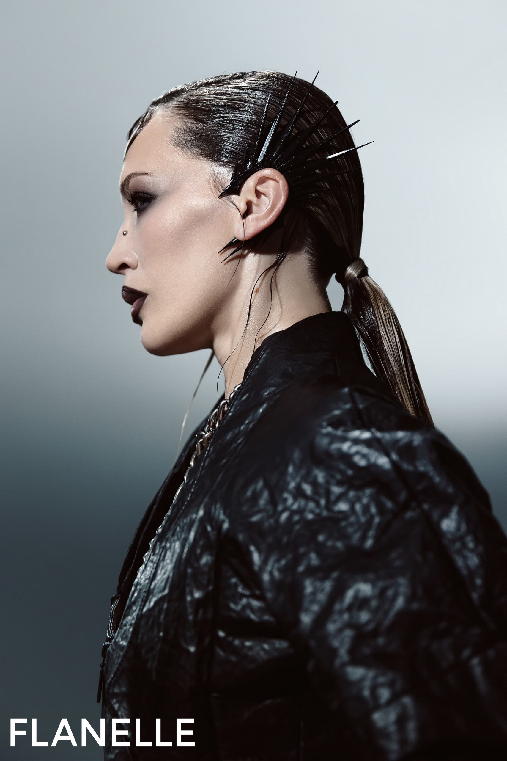 Model with sleek hairstyle and edgy accessories in a dramatic fashion pose.