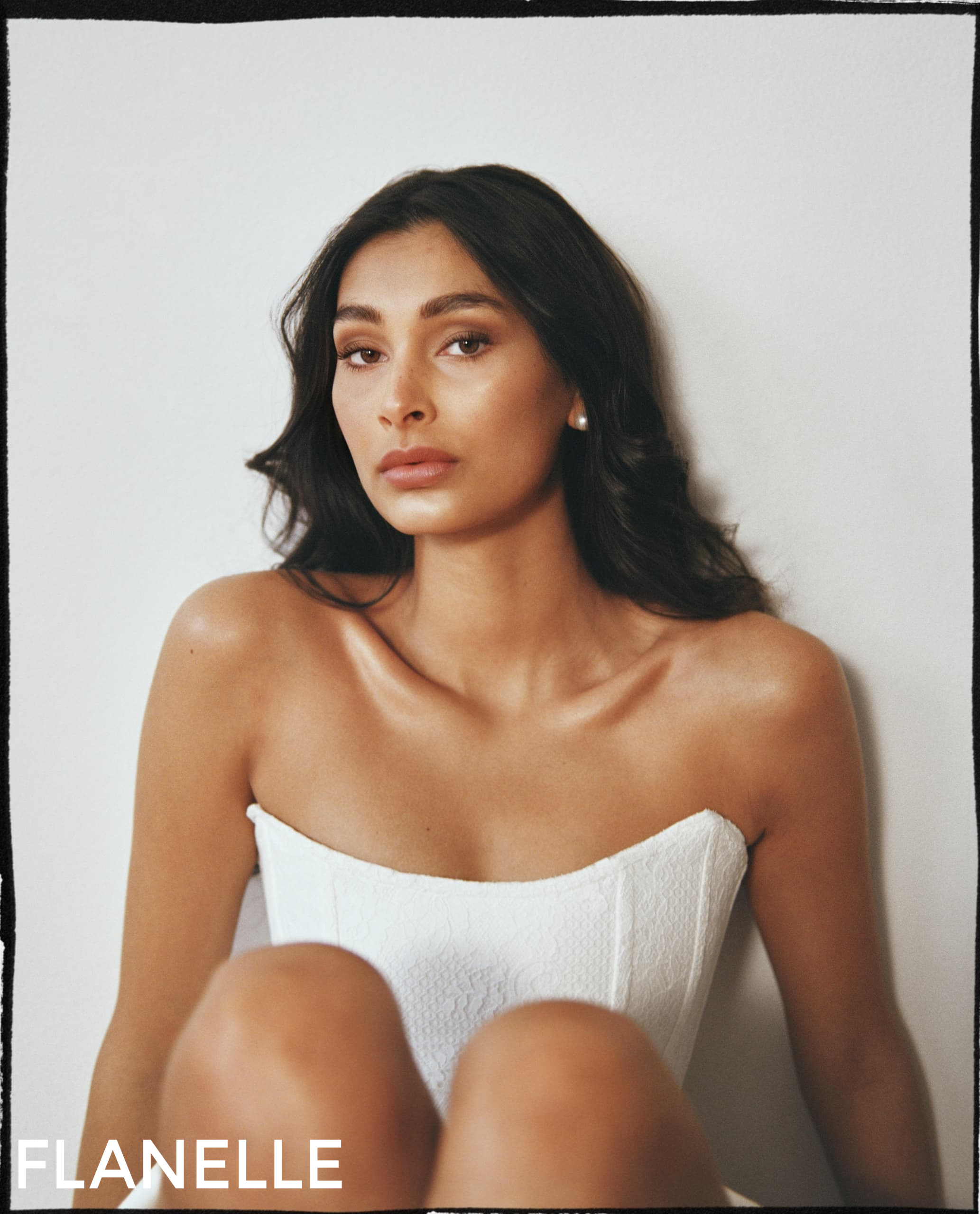Model in strapless white top, sitting against a white wall, Flanelle branding visible.