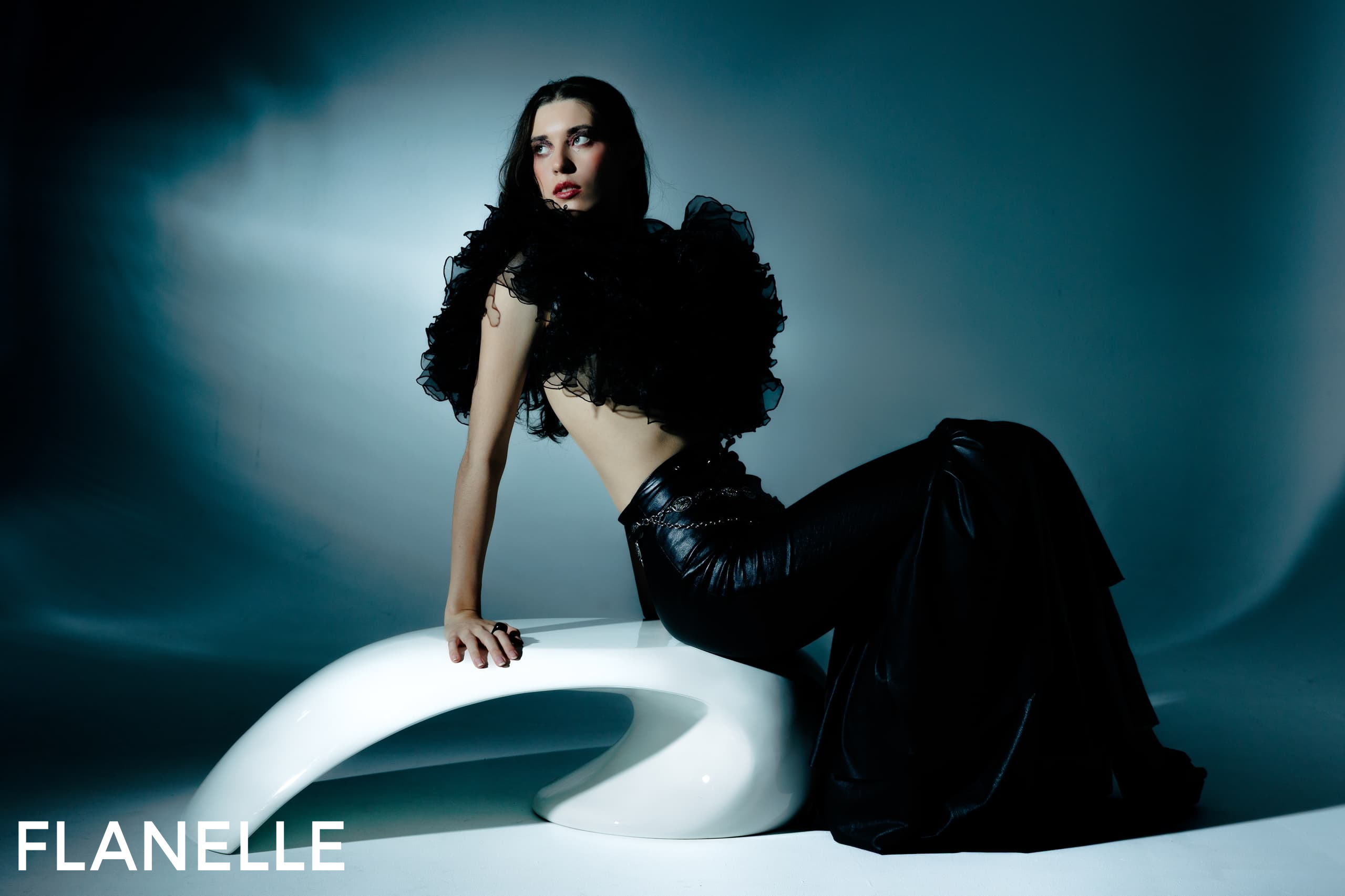 Fashion model in elegant black outfit posing on modern white seat.