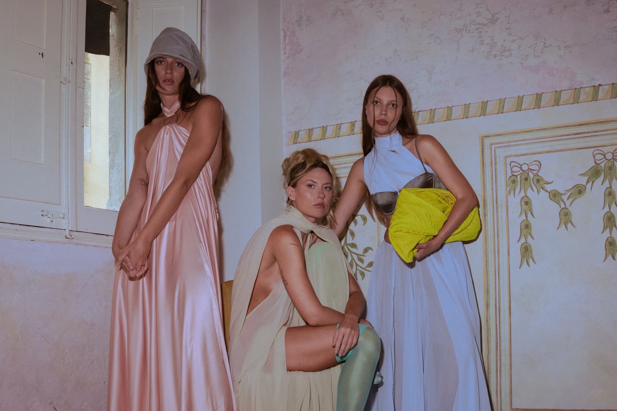 Three women in elegant dresses posing in a stylish, vintage-inspired room.