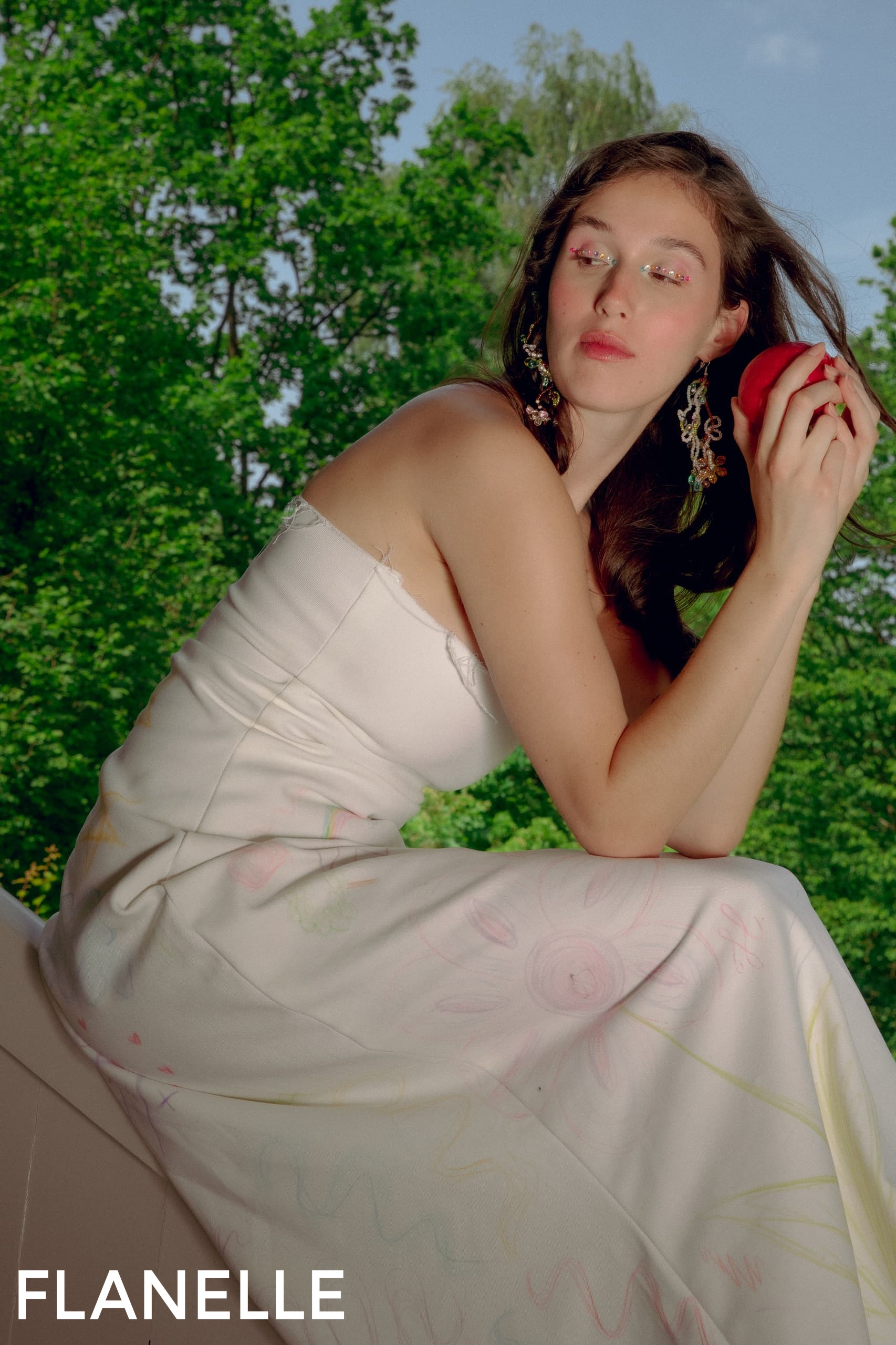 Woman in white dress with floral design in a lush green outdoor setting.