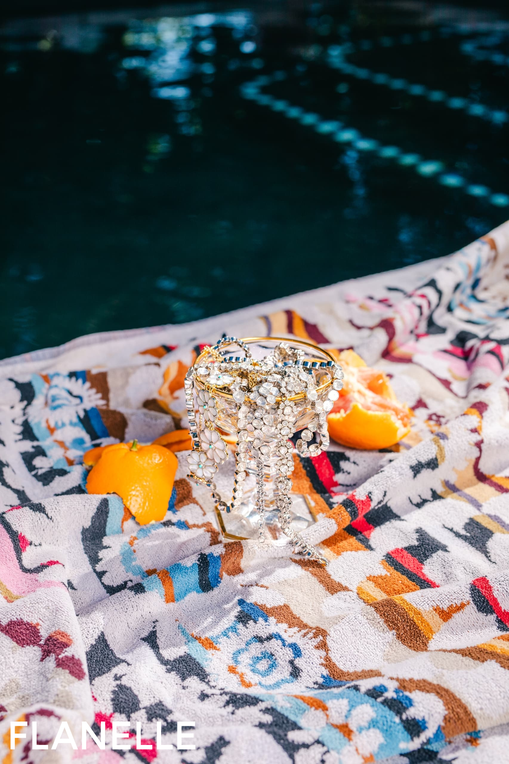 Sparkling jewelry on a patterned towel by the poolside with orange slices.