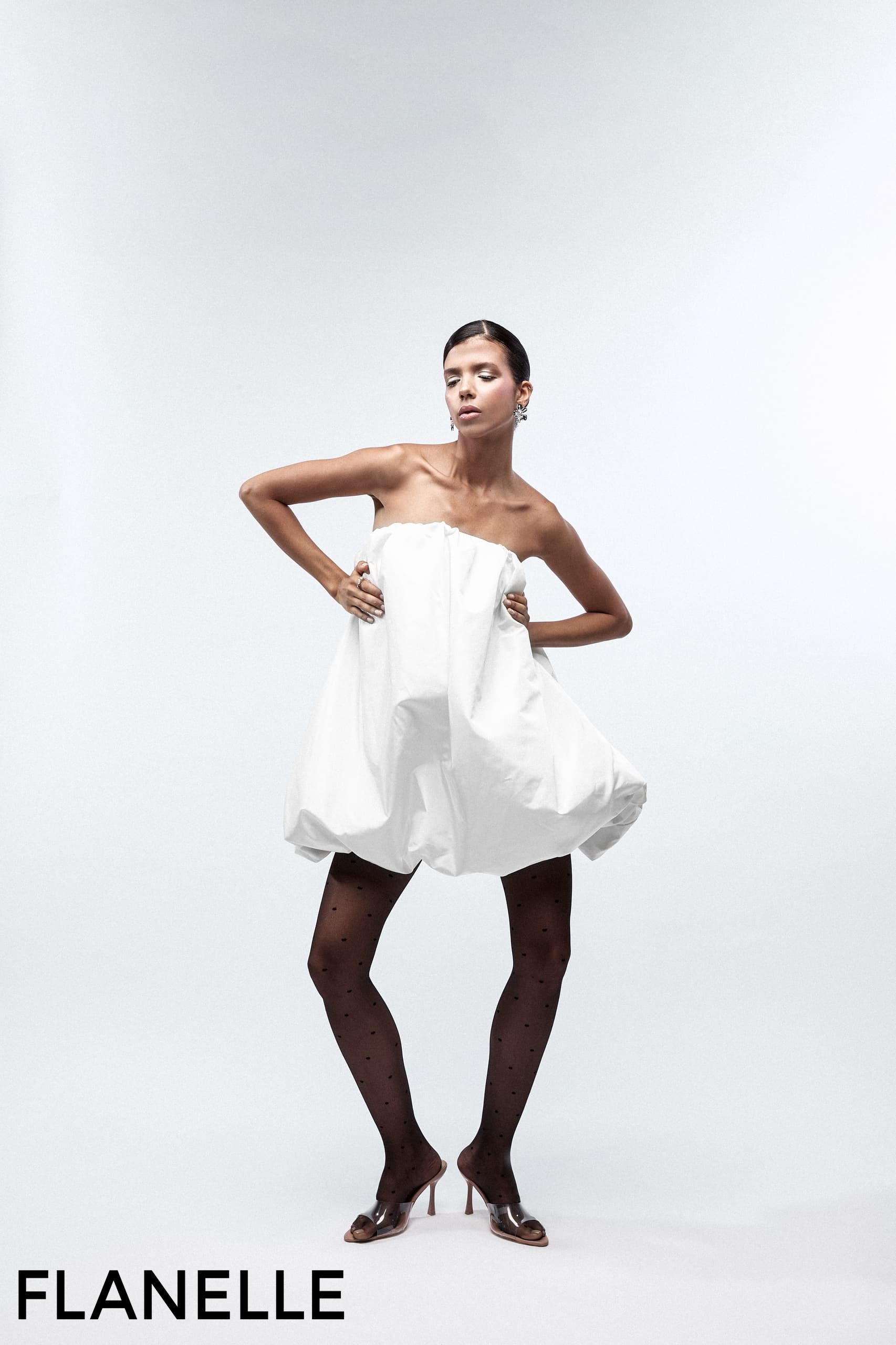 Fashion model in a unique white dress and black polka dot tights by Flanelle.