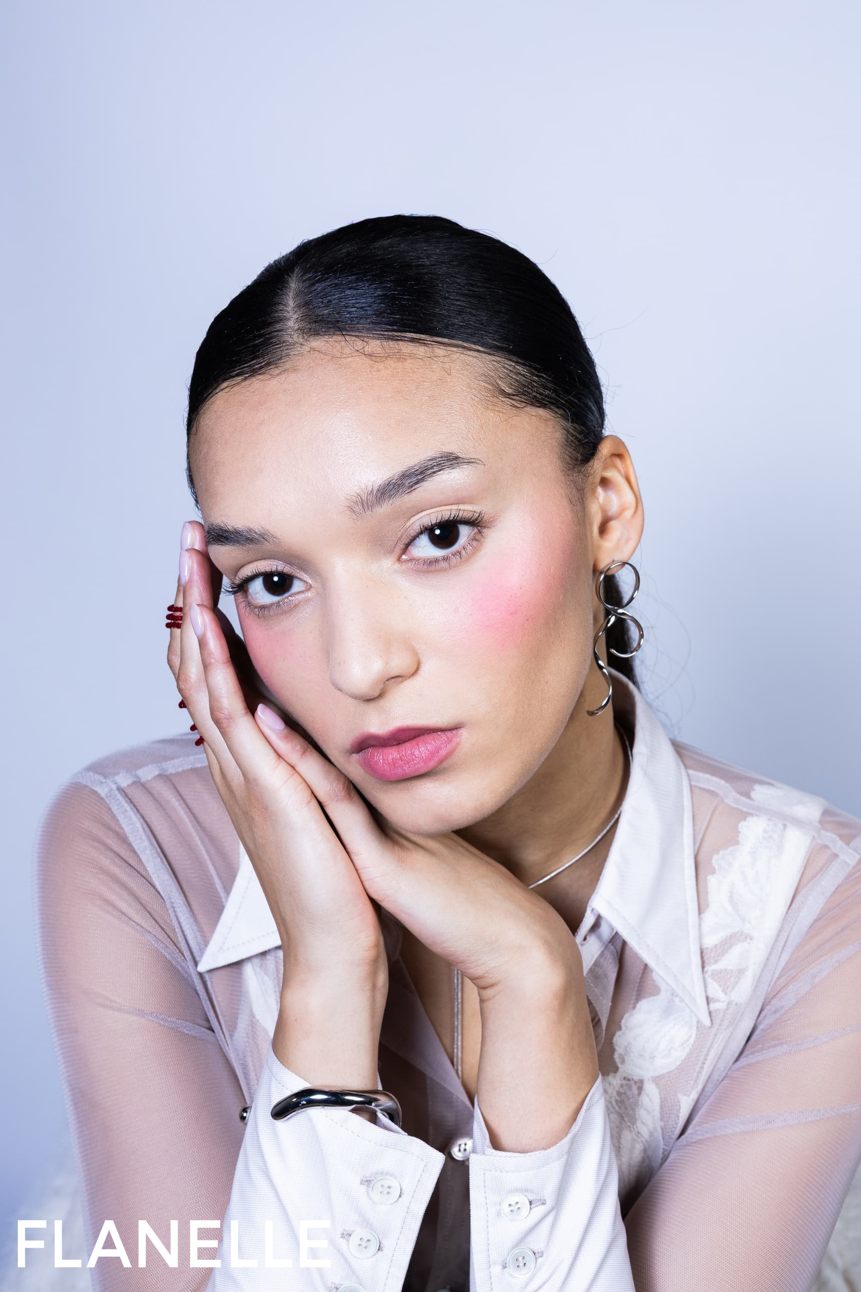 Portrait of a woman posing with hands on face, wearing elegant jewelry and blouse.