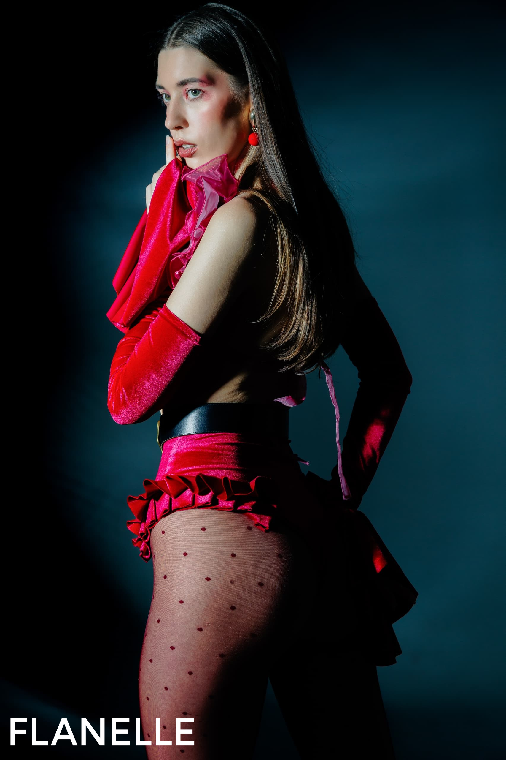 Model in vibrant red fashion ensemble, polka-dot tights, dramatic look.