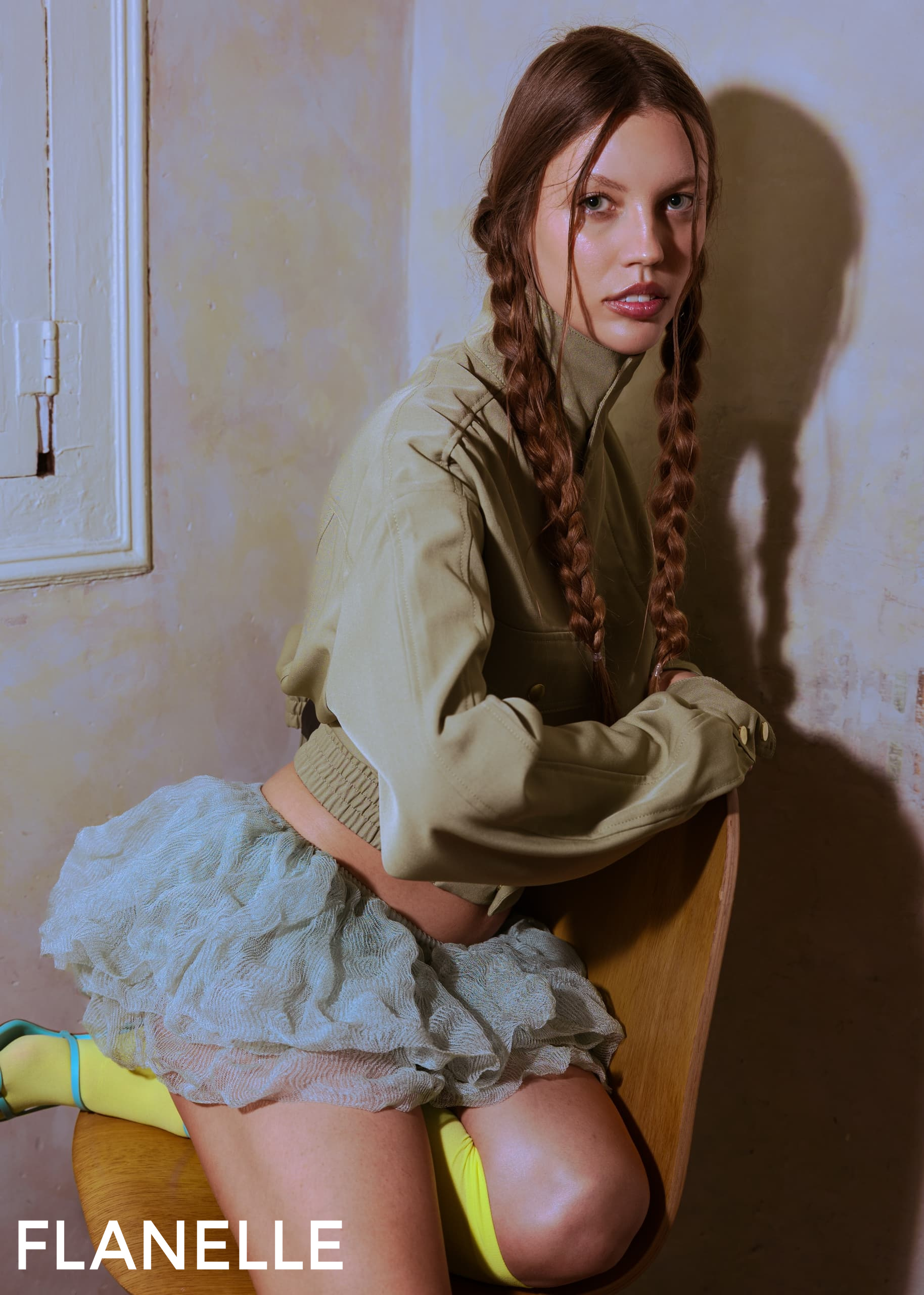 Woman with braids poses in stylish outfit on chair indoors.