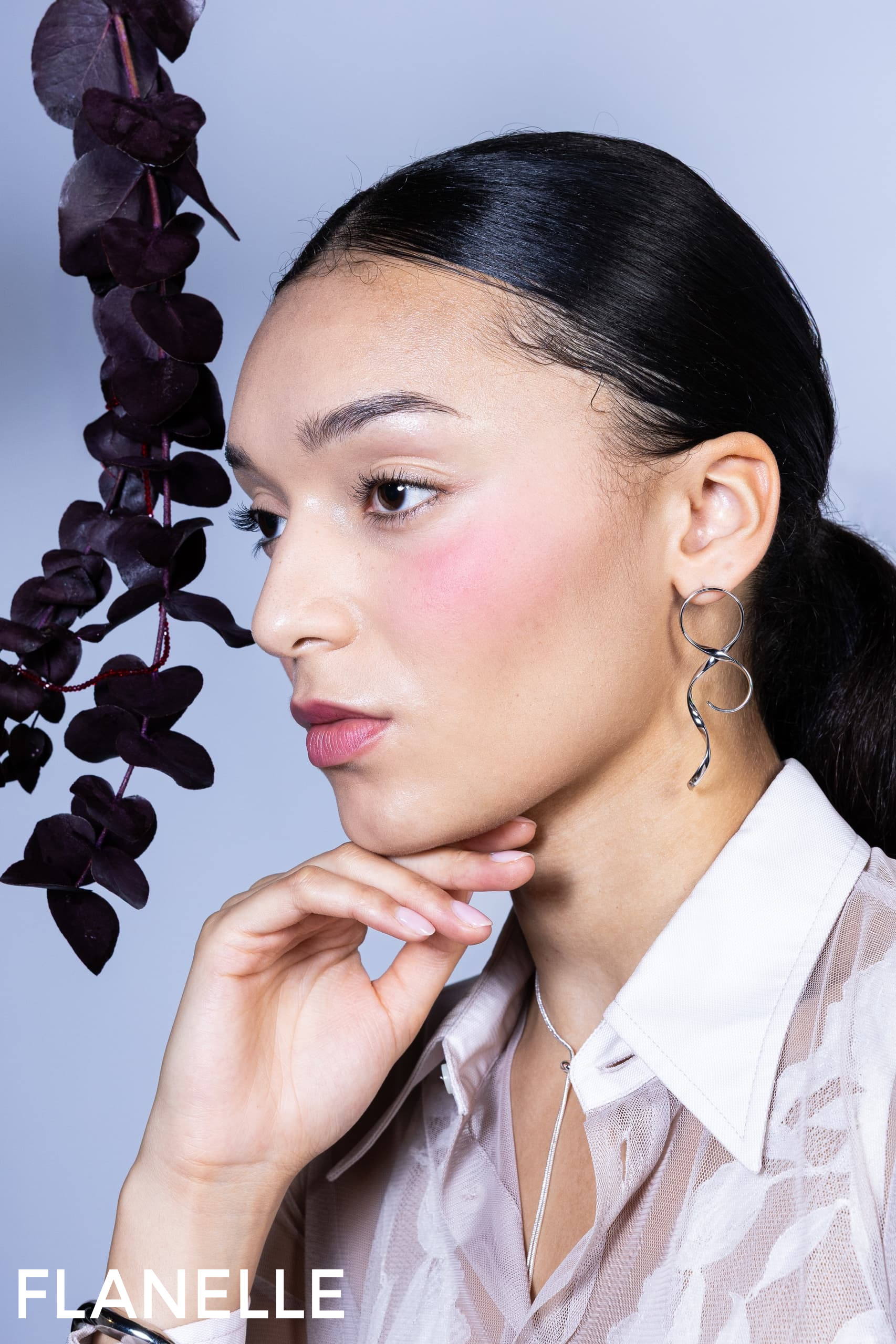 Model with silver earrings and floral backdrop; elegant fashion portrait.