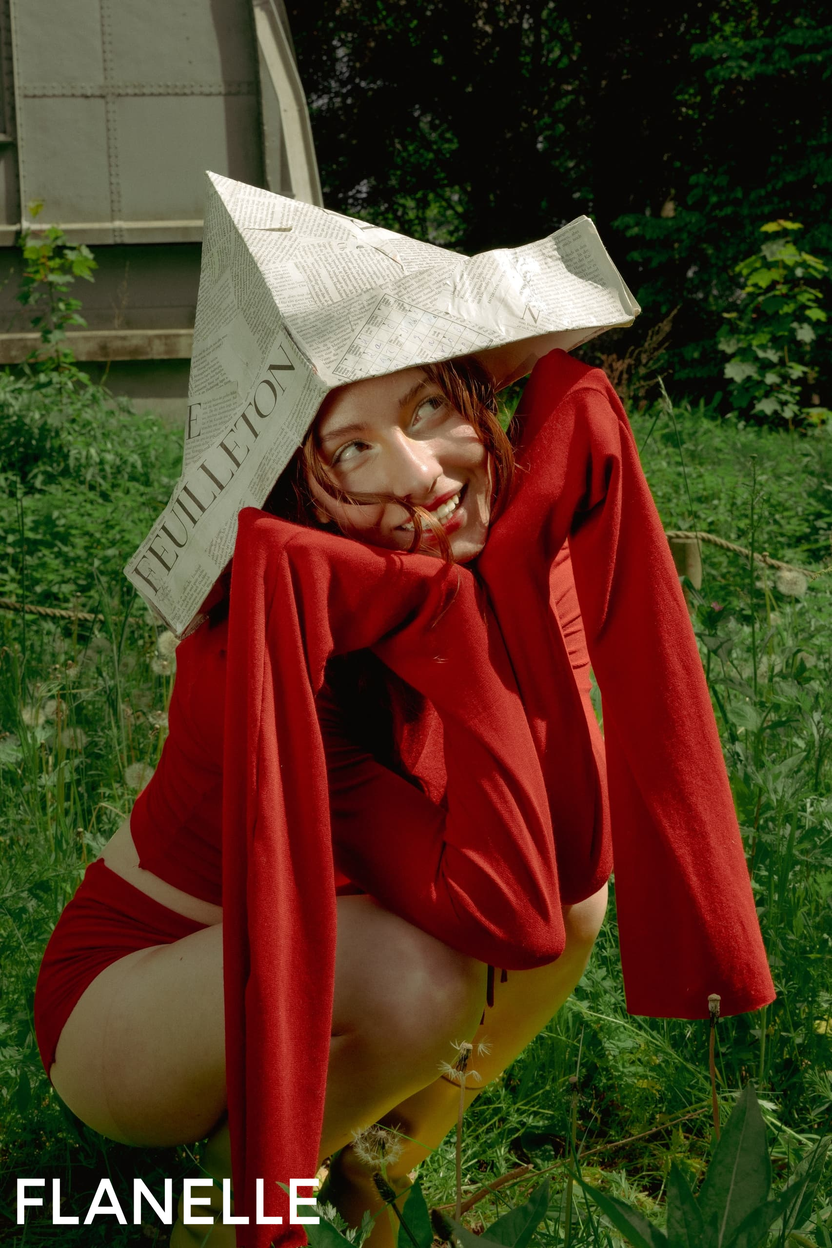 Woman in red outfit with a newspaper hat in a lush green garden.