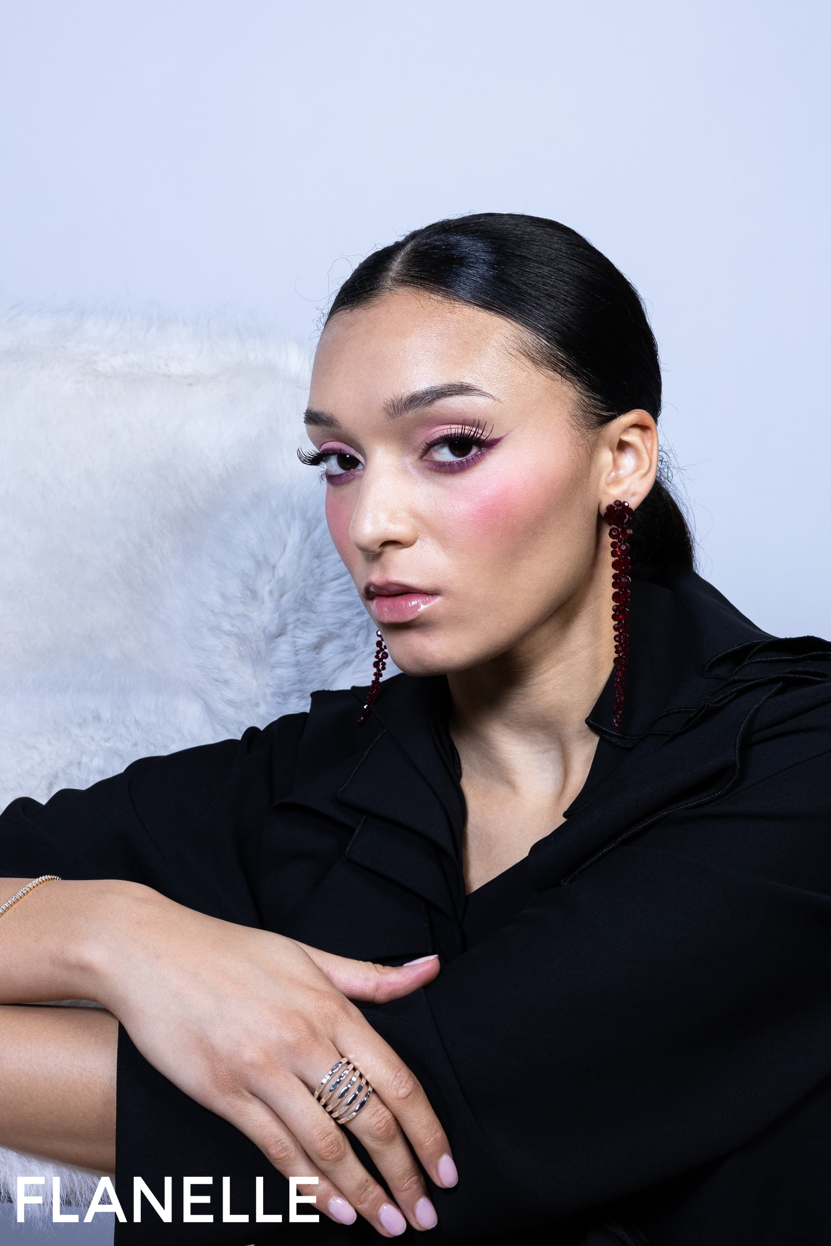 Elegant woman with bold makeup and stylish earrings, posing in black attire.