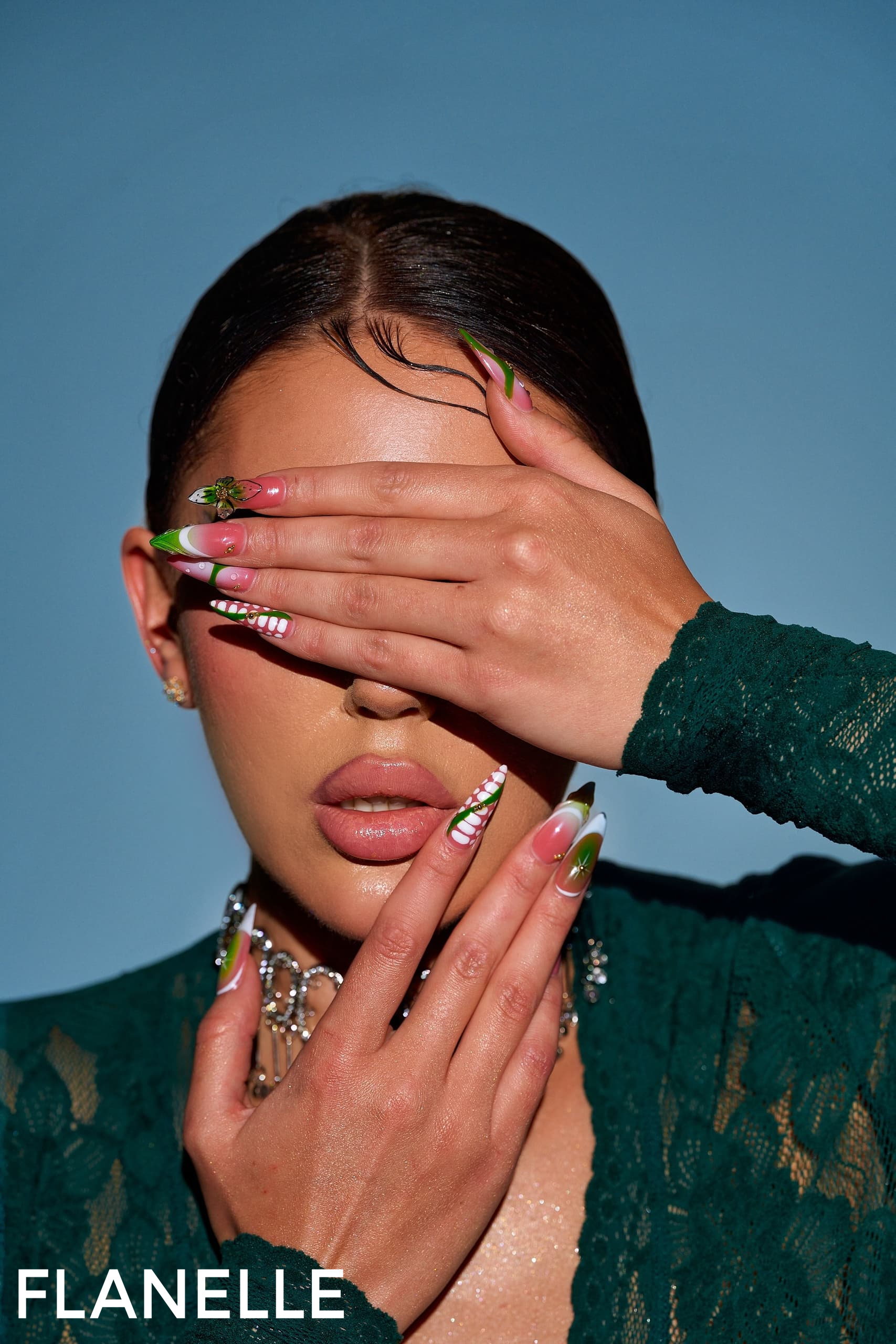 Model with intricate green nail art covers face, wearing green lace outfit.
