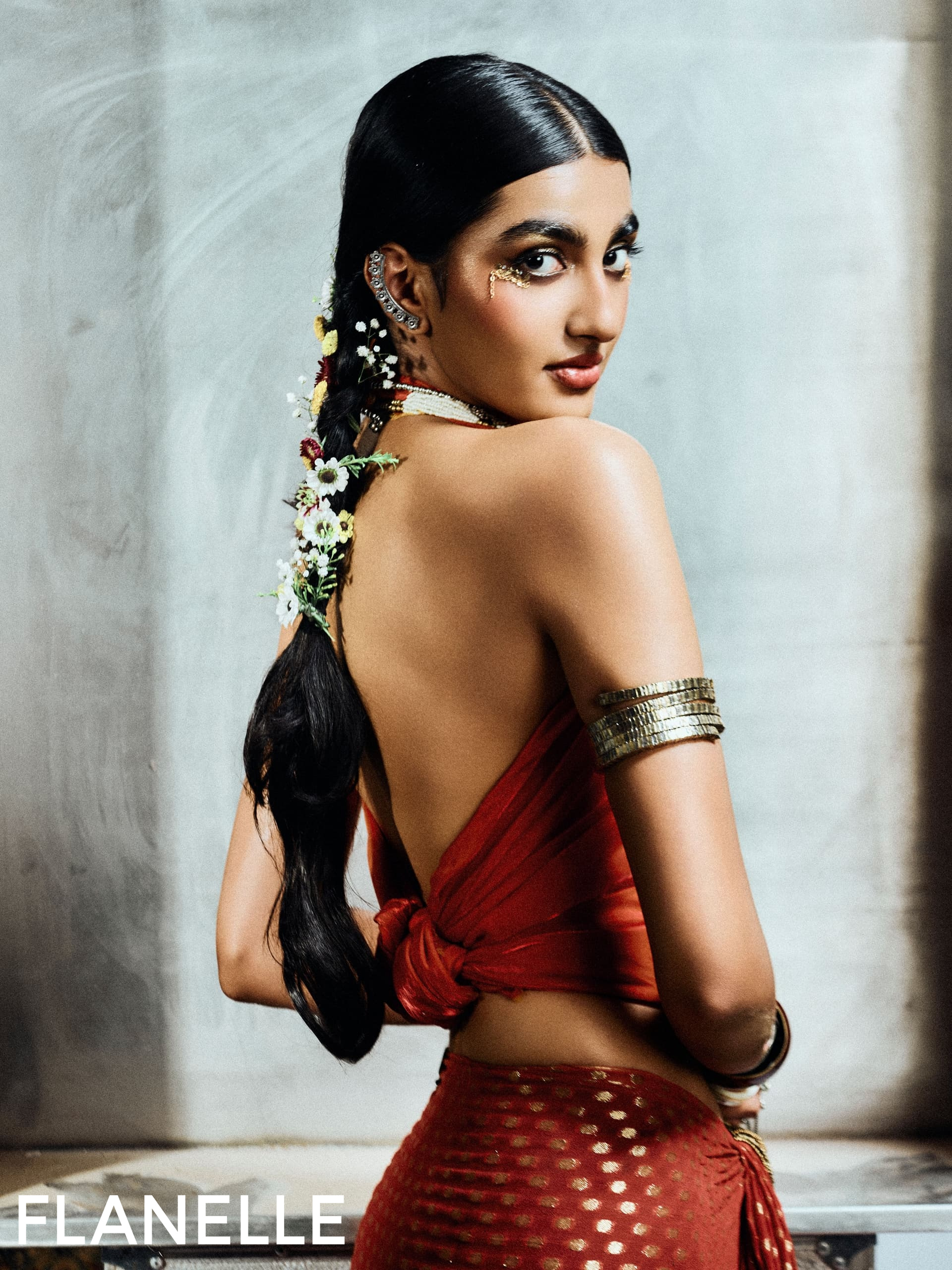 Woman in elegant red outfit, adorned with flowers and jewelry, looking back.