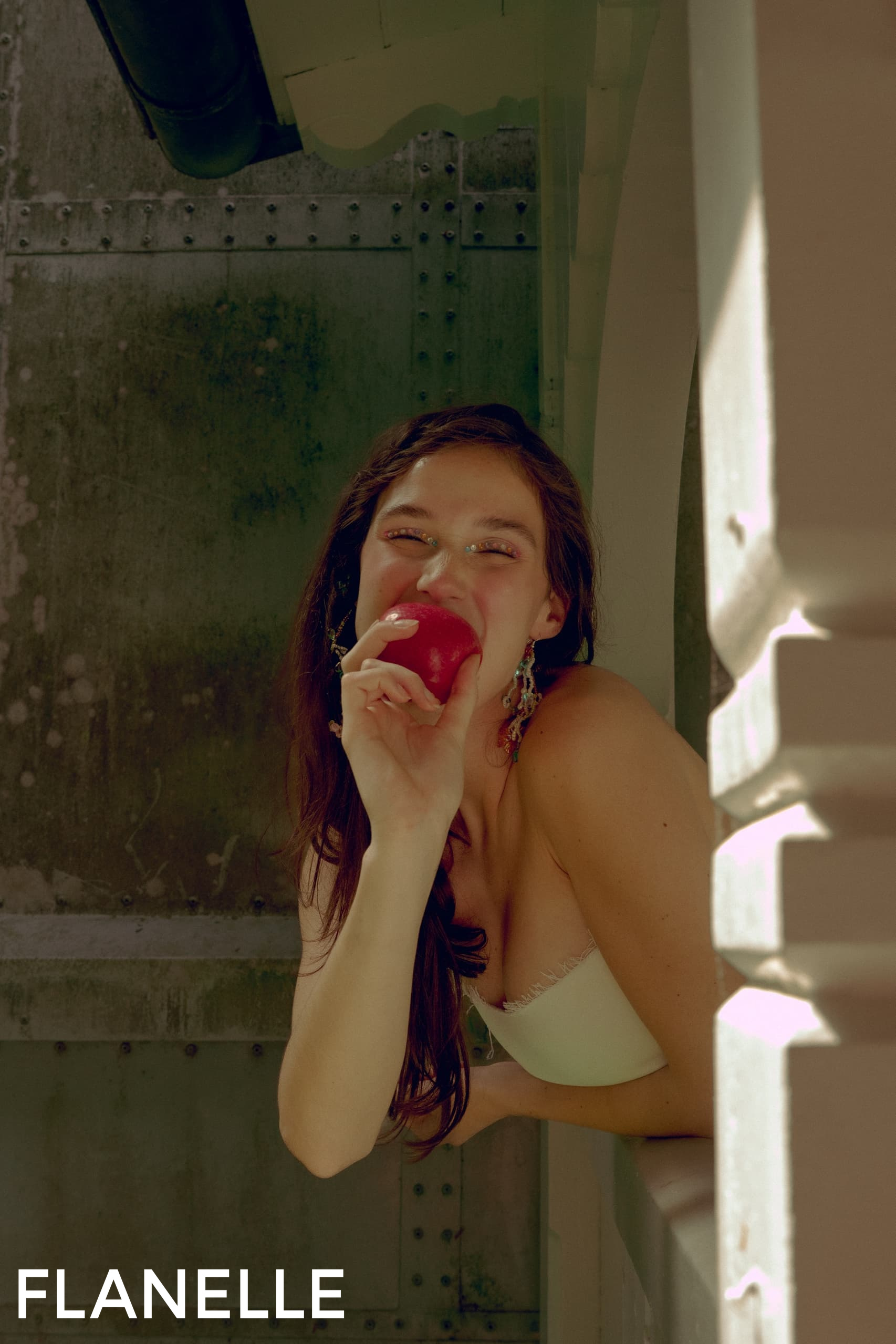 Woman enjoys a red apple while smiling in natural light.