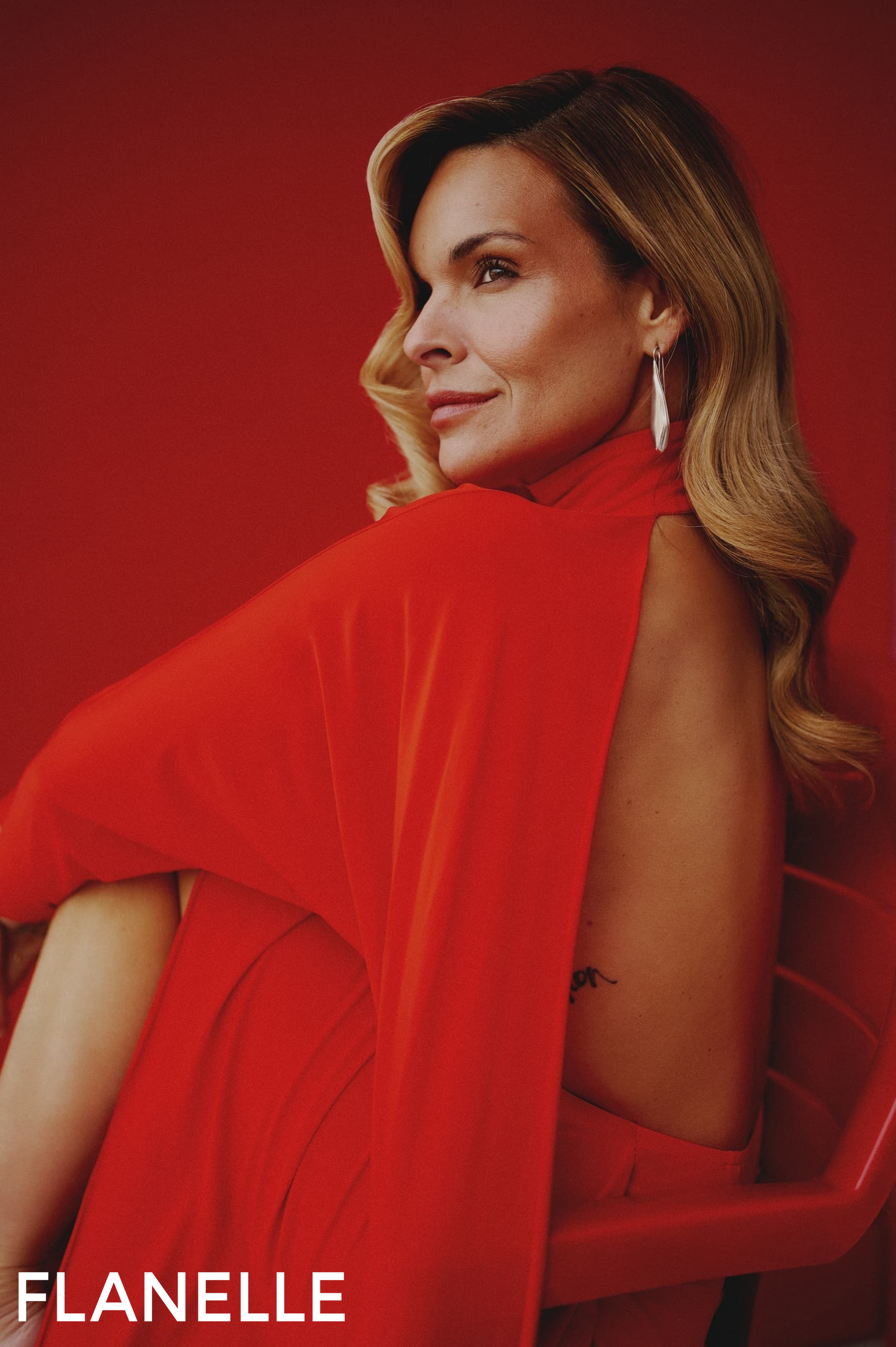 Woman in red backless dress with elegant updo hairstyle against red background.