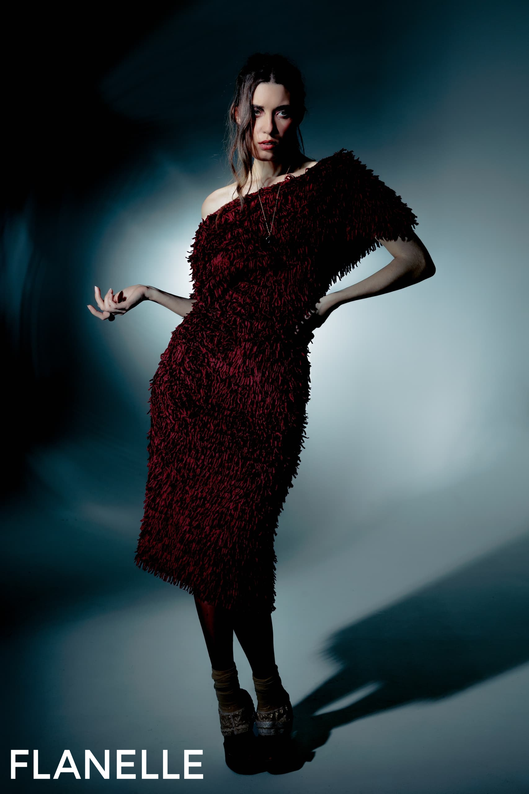 Fashion model in a textured burgundy dress, posing under moody lighting.
