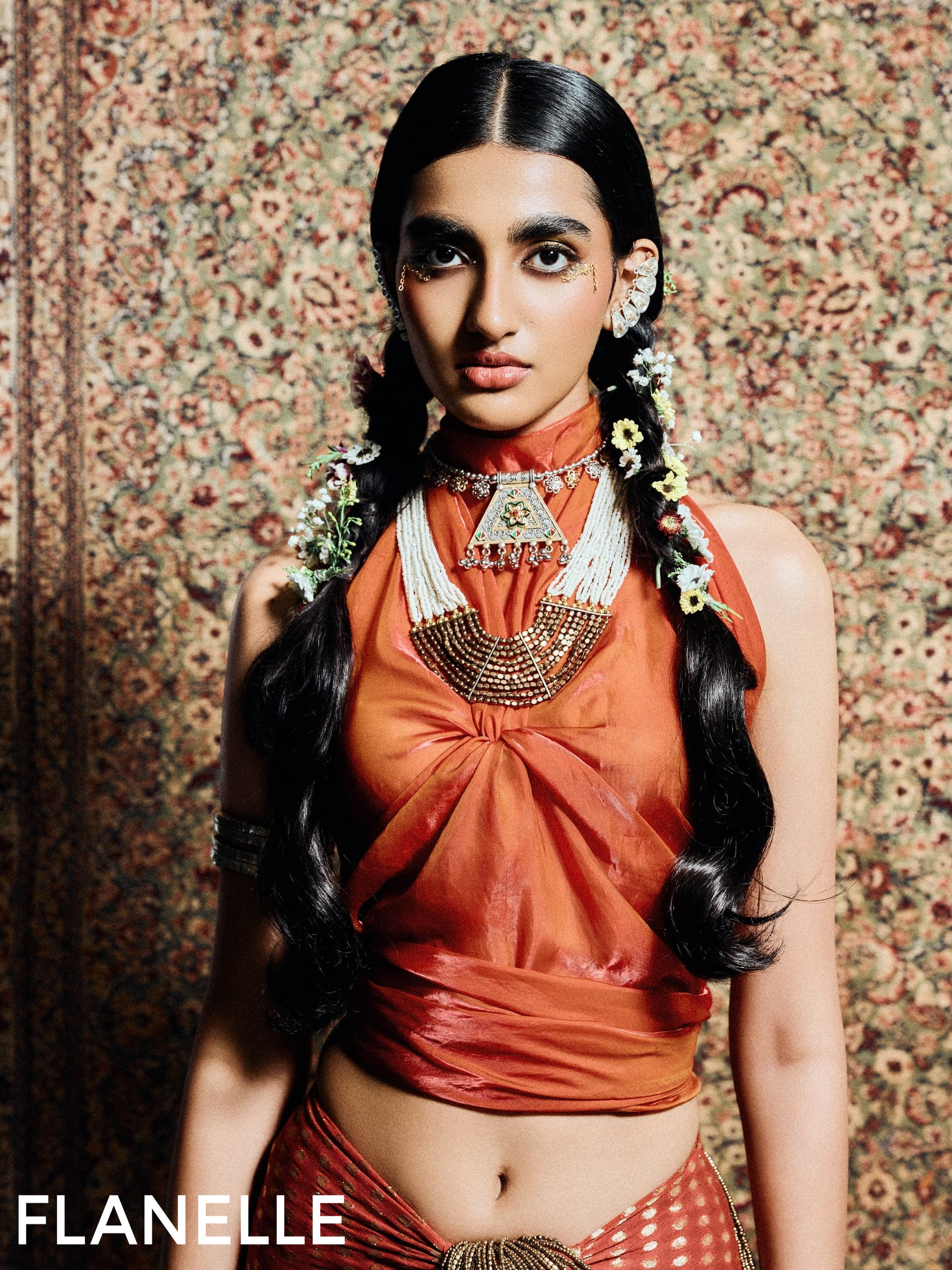 Fashion model in ornate jewelry and orange attire with floral accents. Flanelle photoshoot.