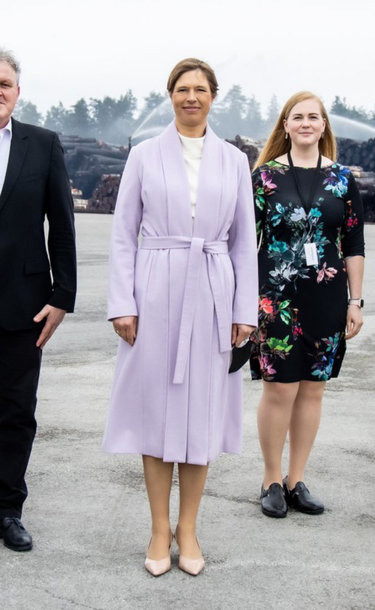 Three people standing outdoors, wearing formal clothing with a forest backdrop.