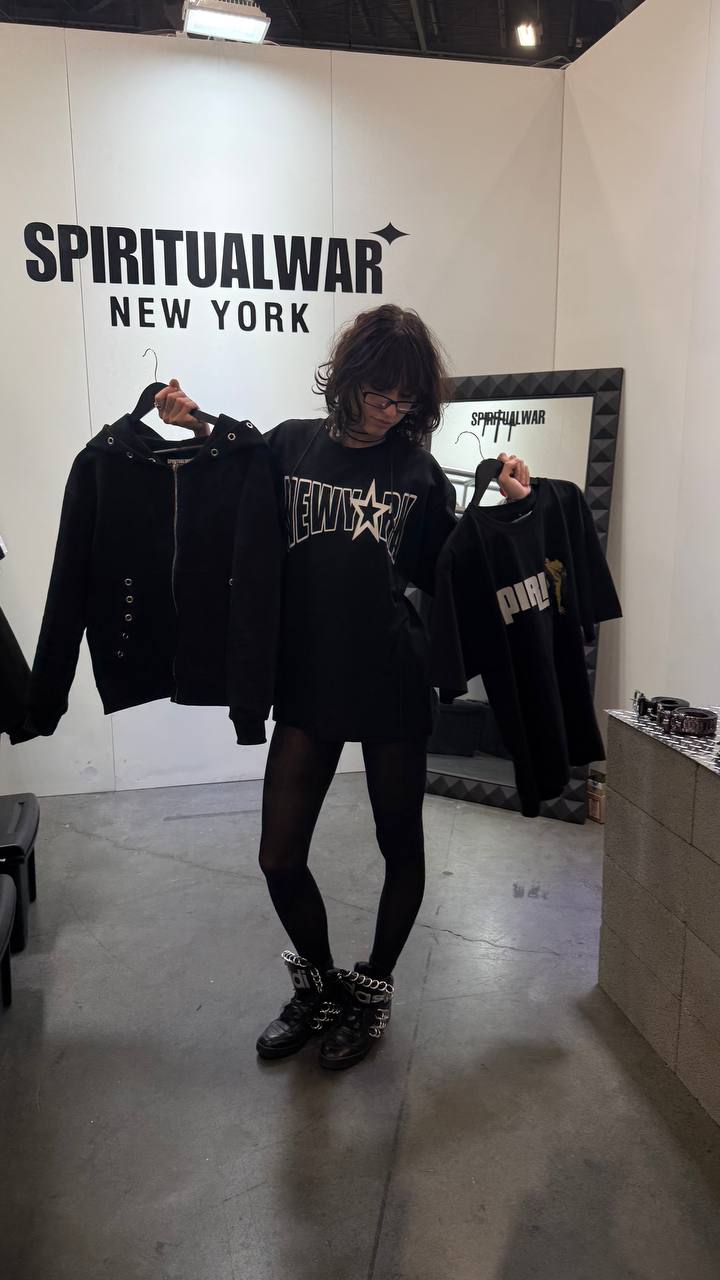 Person showcasing SpiritualWar New York apparel at a fashion booth.