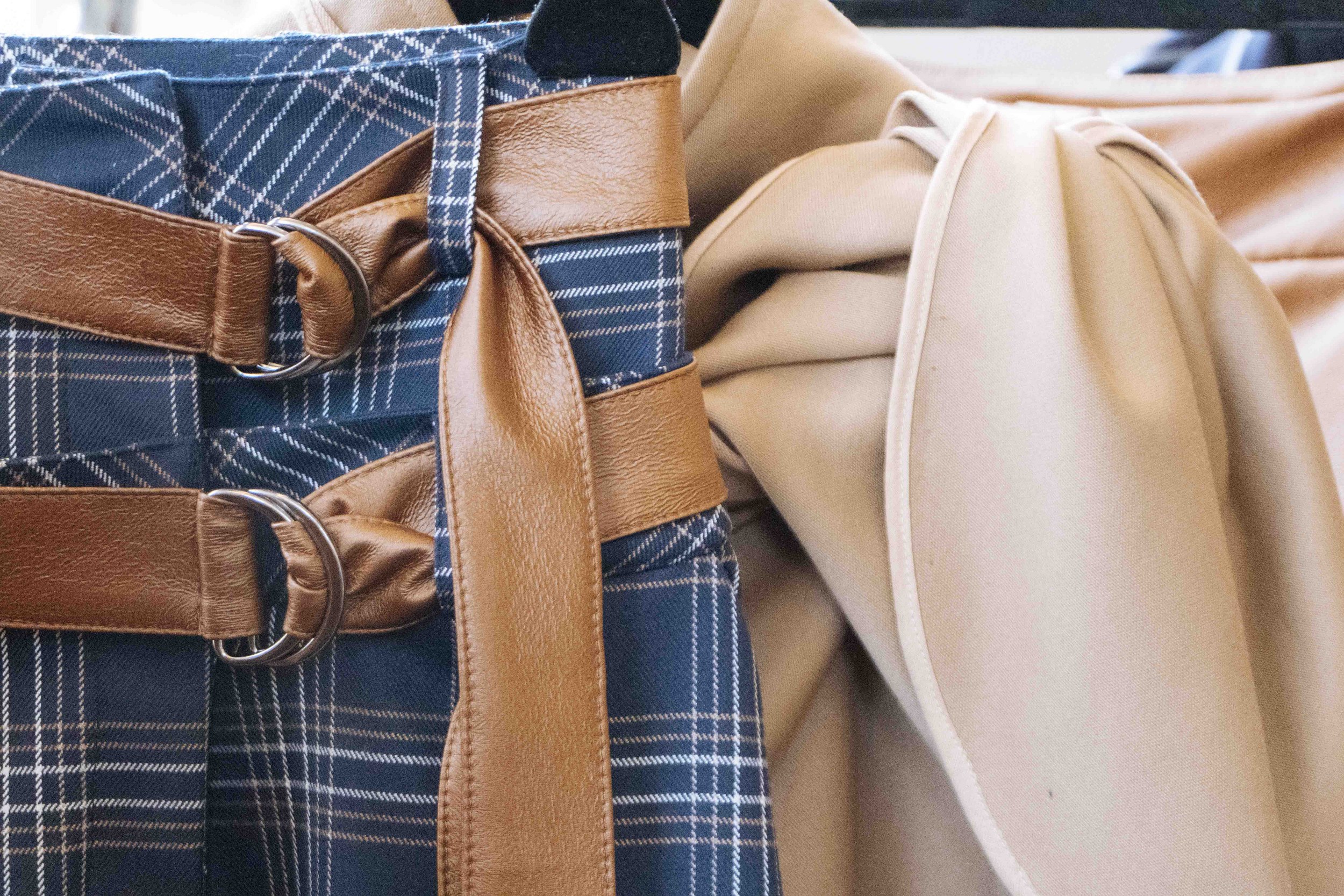 Plaid skirt with leather belts and beige coat hanging side by side.