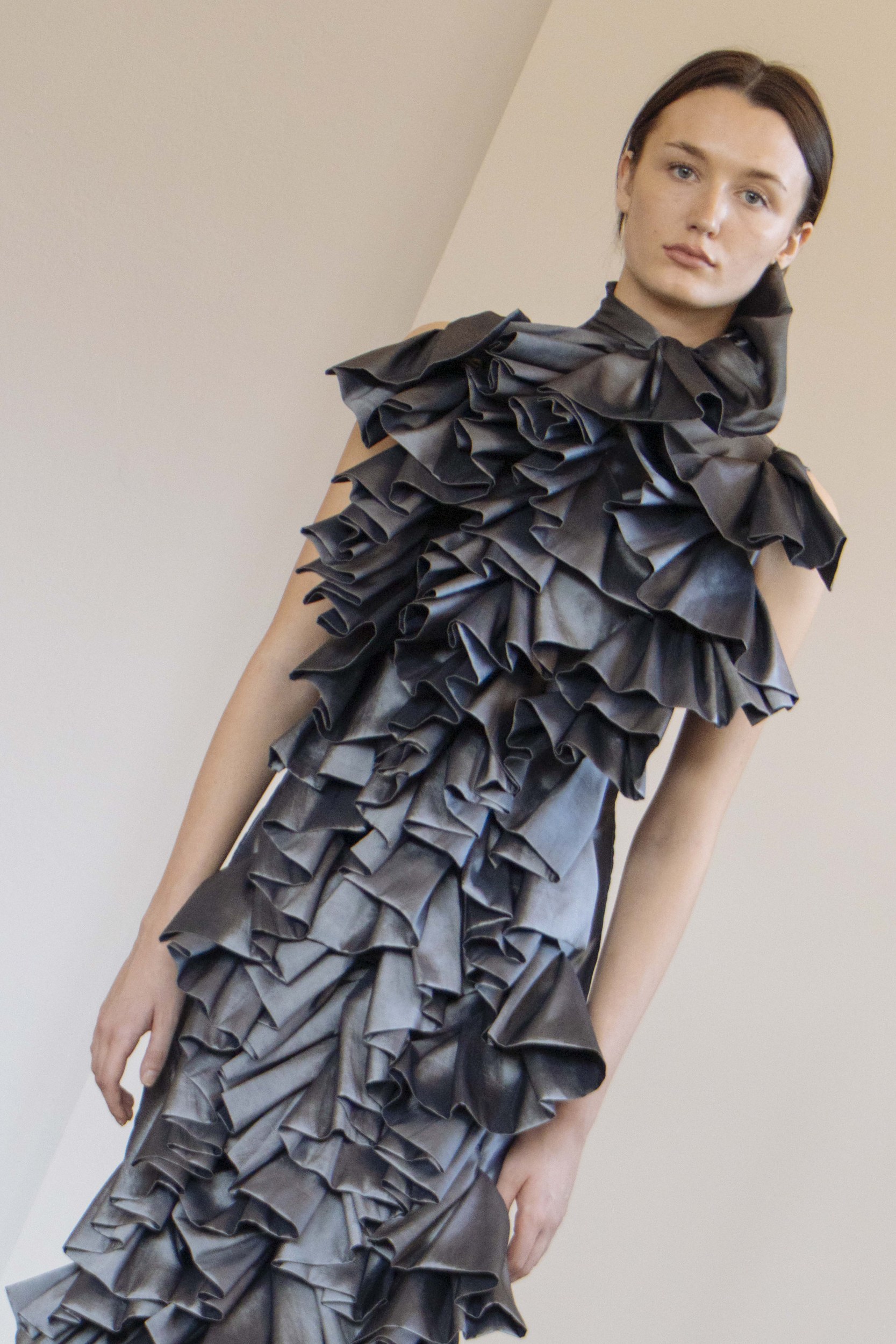 Model in a black ruffled dress showcasing avant-garde fashion design.