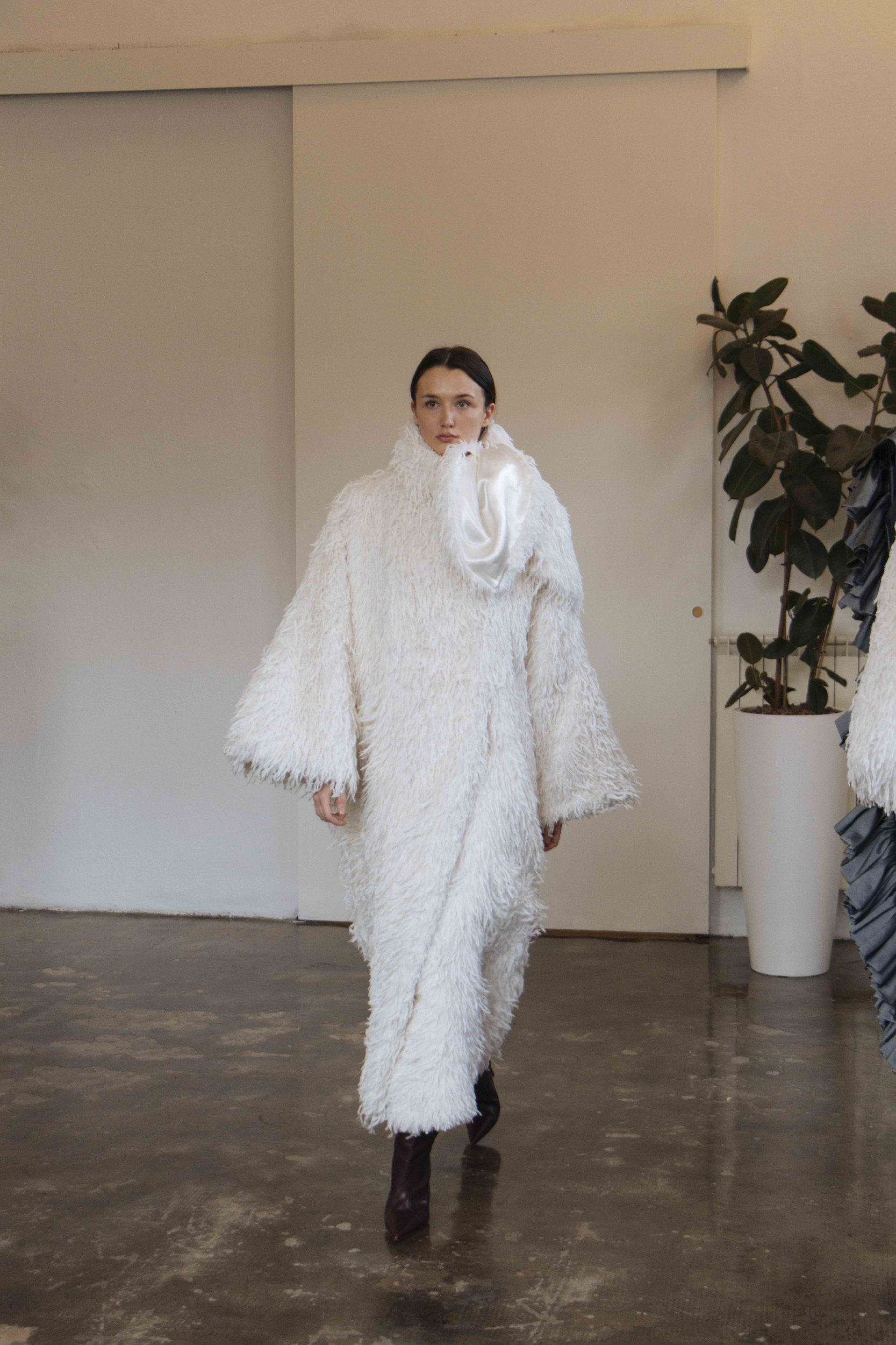 Model in fluffy white coat with stylish high collar on runway.
