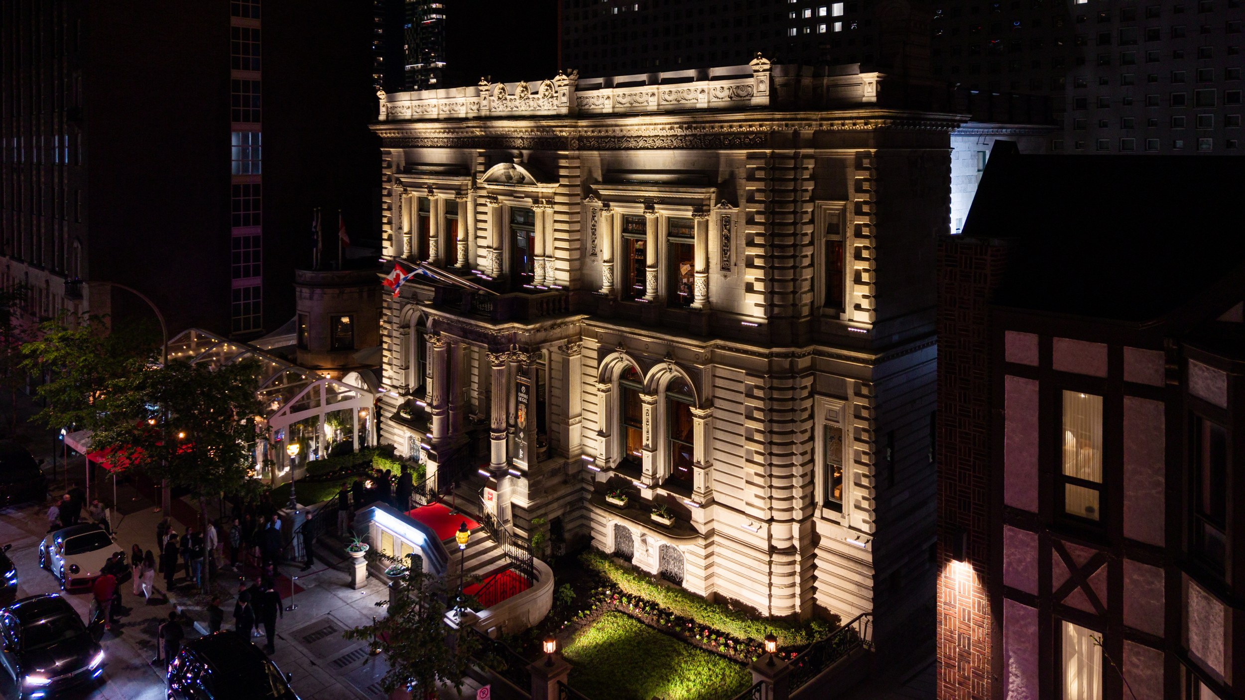 Illuminated historic city building at night with people gathered outside.
