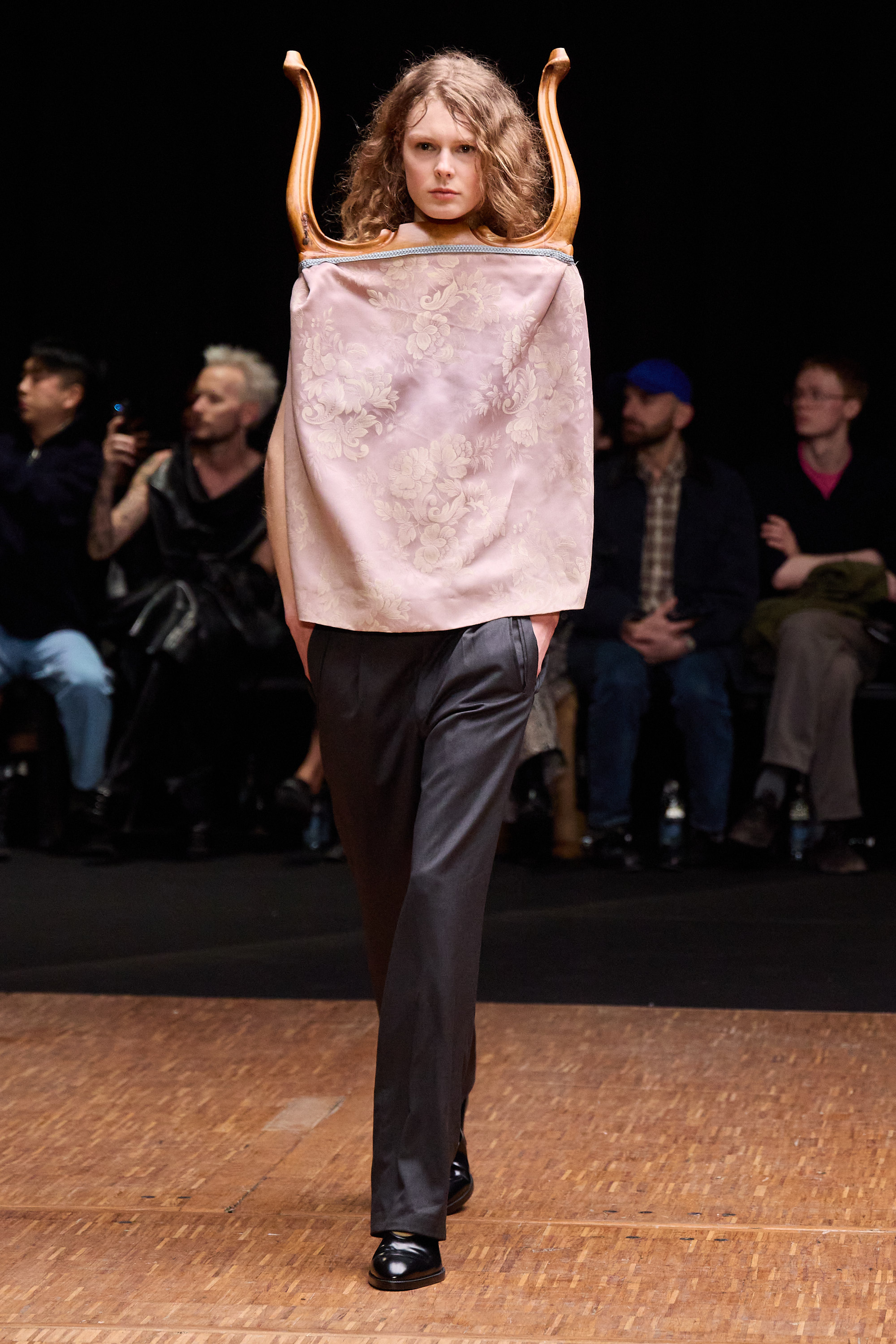Fashion model on runway in unique attire with chair-back and floral fabric.