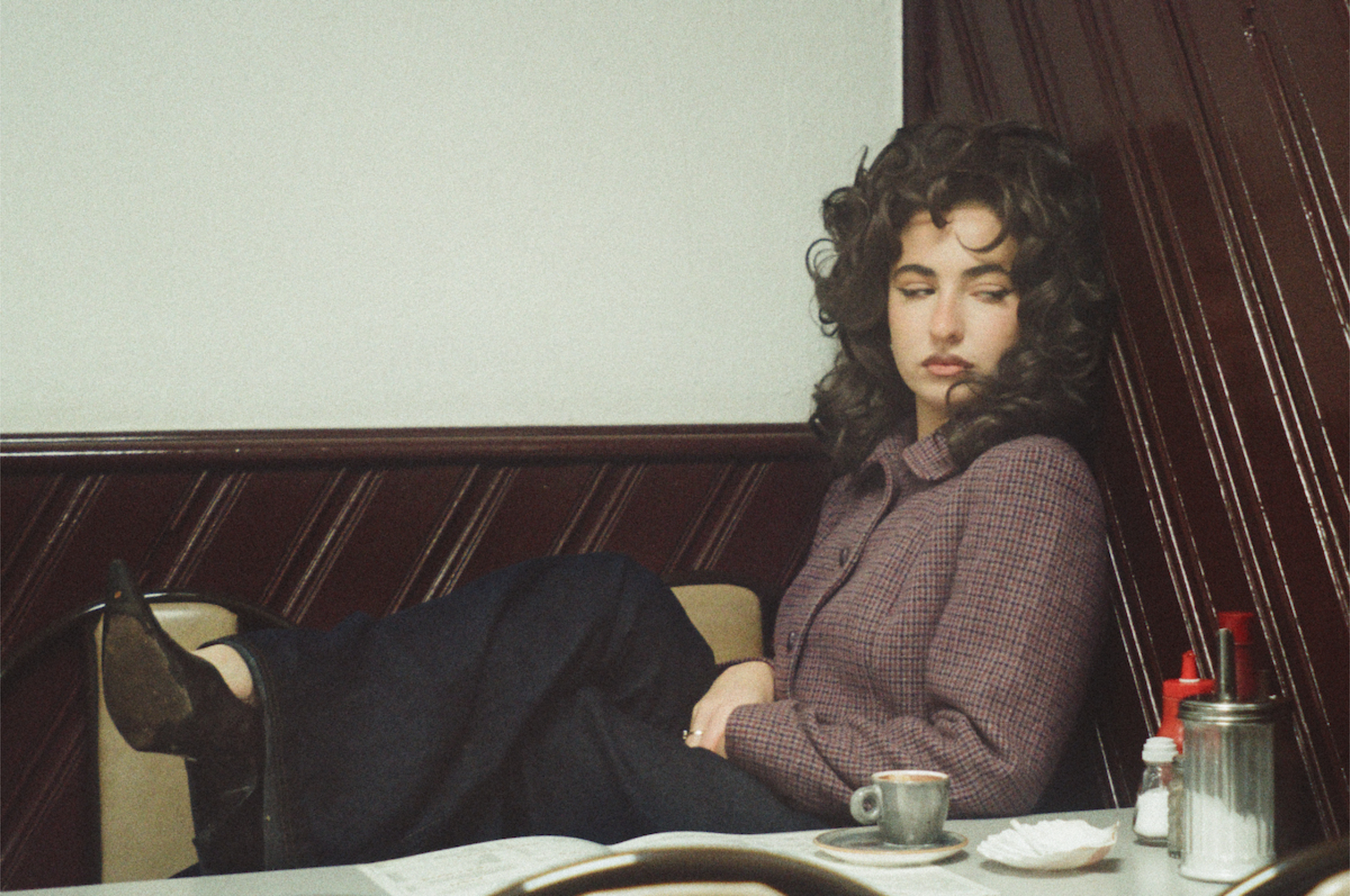 Woman sitting alone in a café booth, vintage style and contemplative mood.