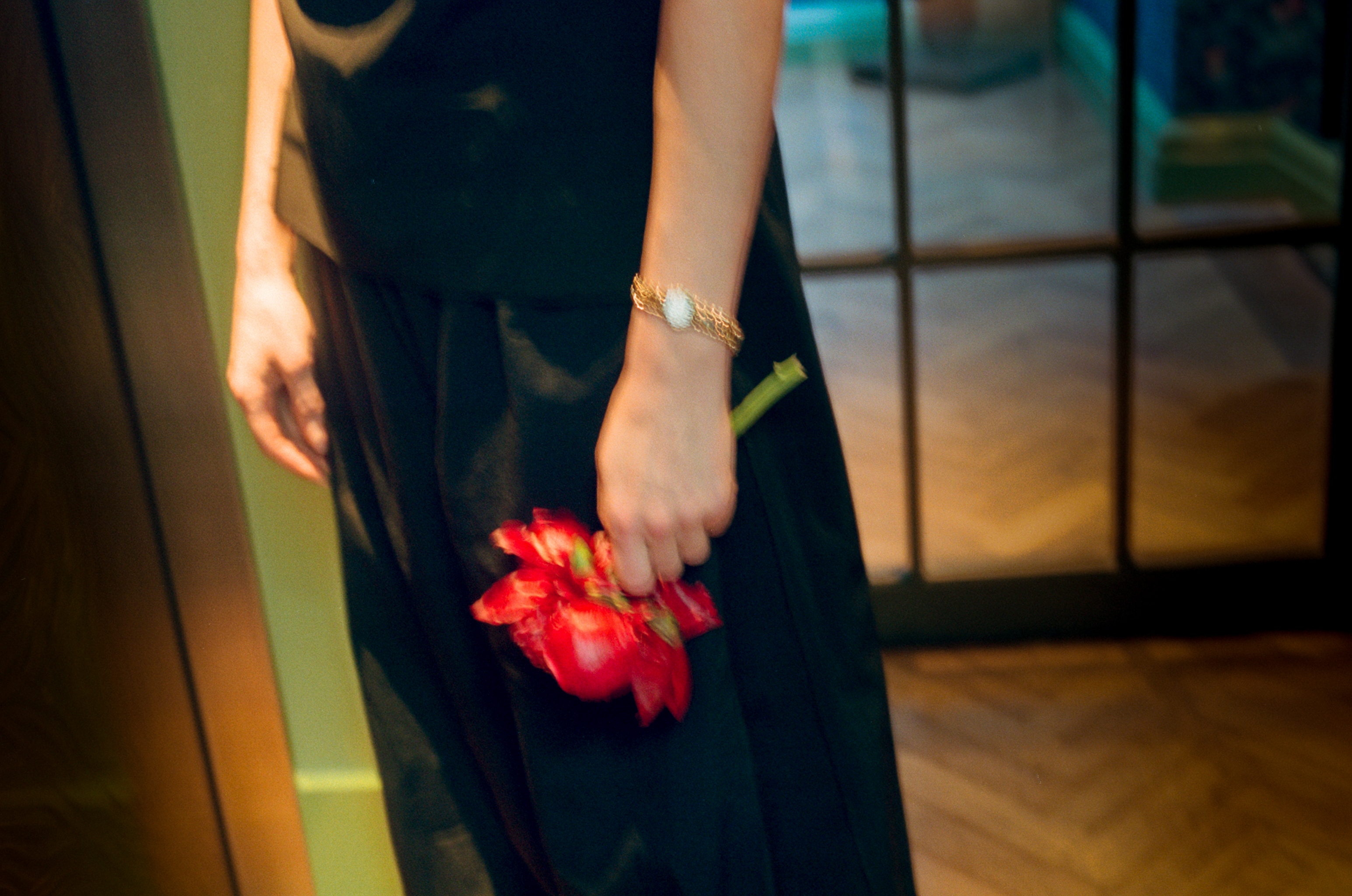 Person holding red flower, wearing elegant black outfit and gold bracelet.