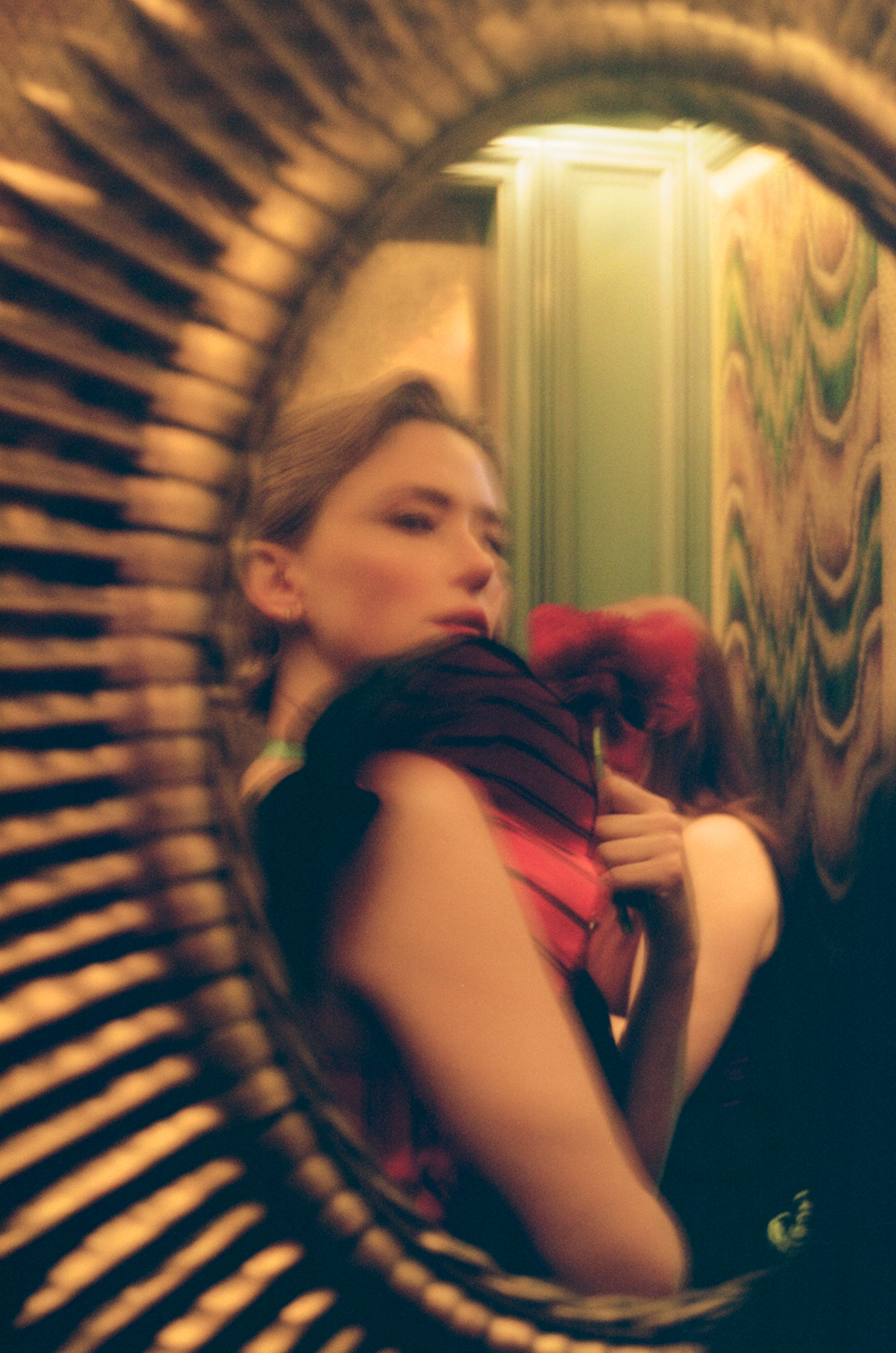 Blurred reflection of a woman holding a flower in a decorative mirror.