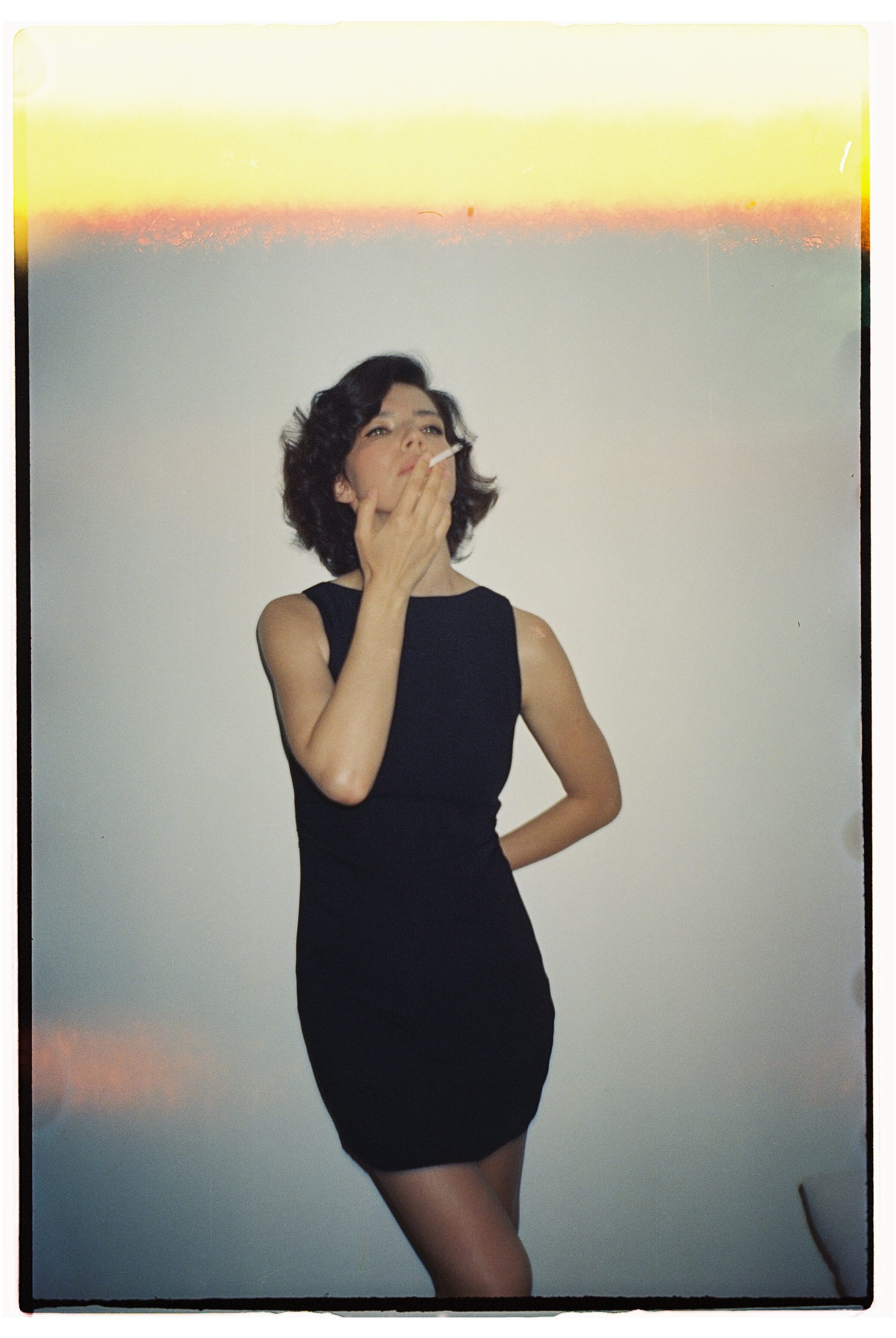 Woman in black dress with vintage vibe, smoking elegantly indoors.